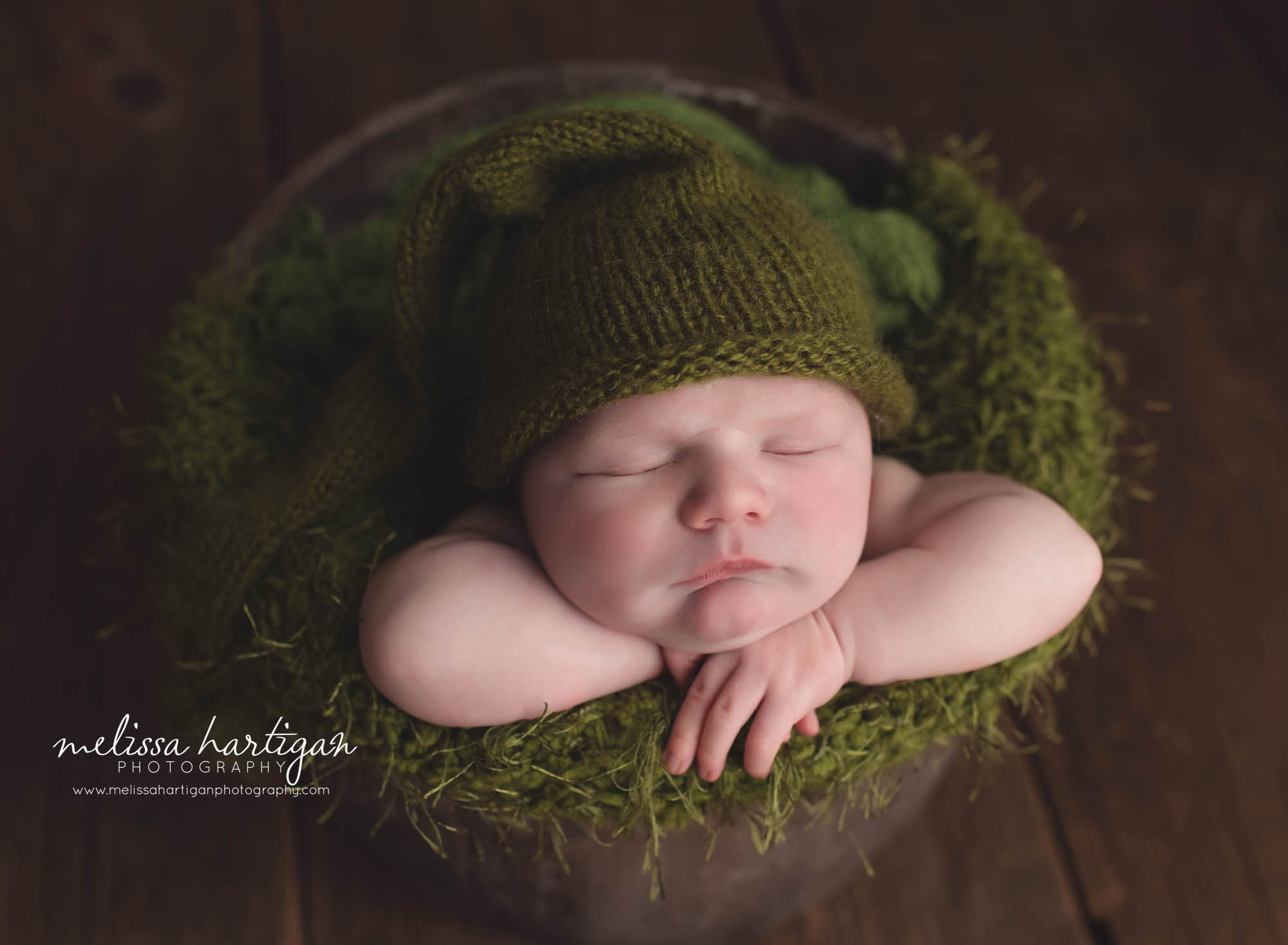 newborn posed in brown bucket with green moss layer
