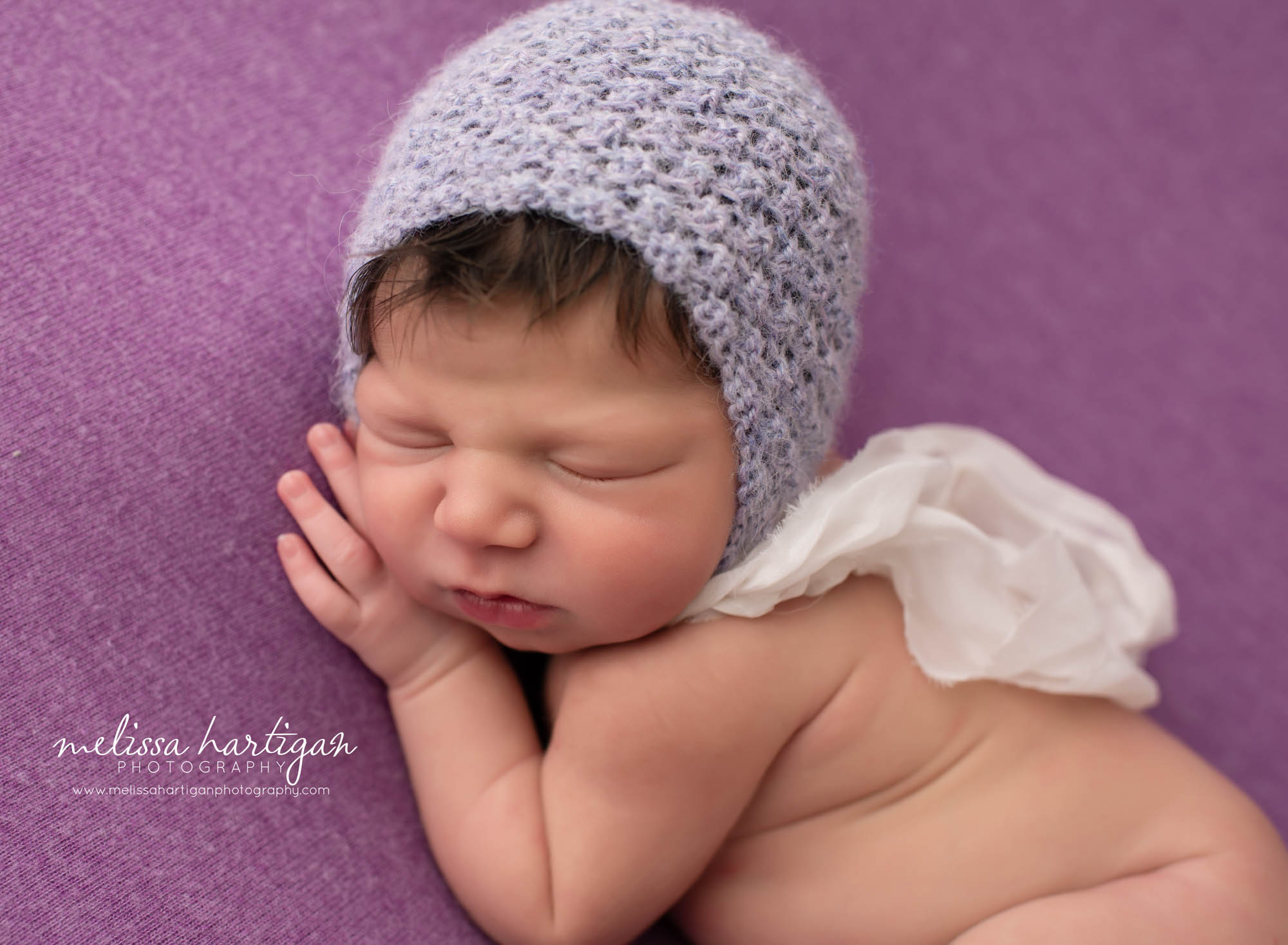 baby girl posed on purple fabric with lilac purple colored knitted bonnet