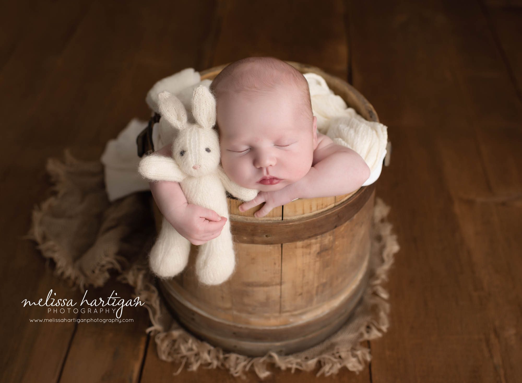 Baby boy holding cream white knitted bunny posed in barrel with head on hands Connecticut newborn photographers