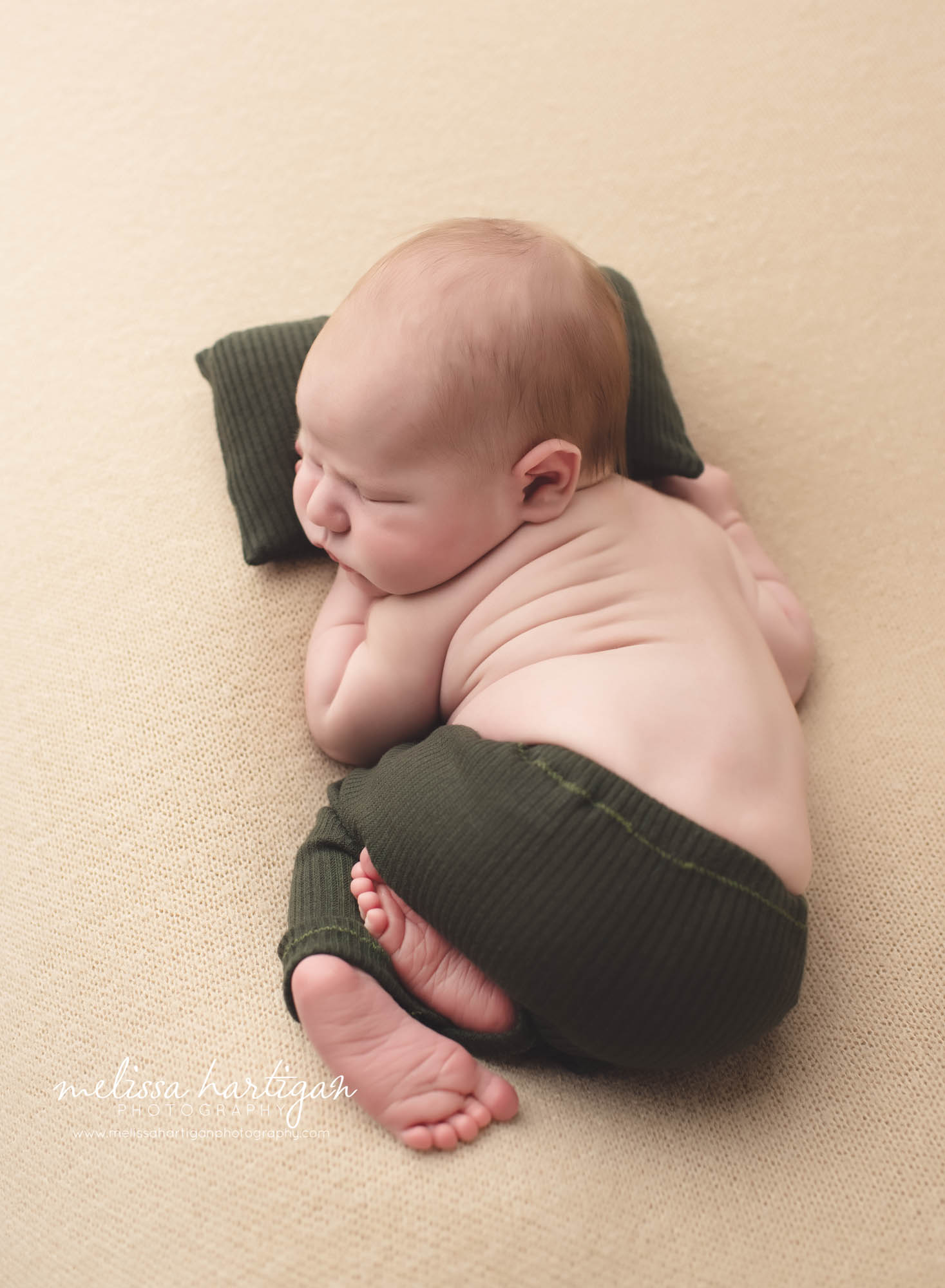 Newborn baby boy sleeping on baby pillow backside up wearing hunter forest green newborn pants Baby Photographer CT