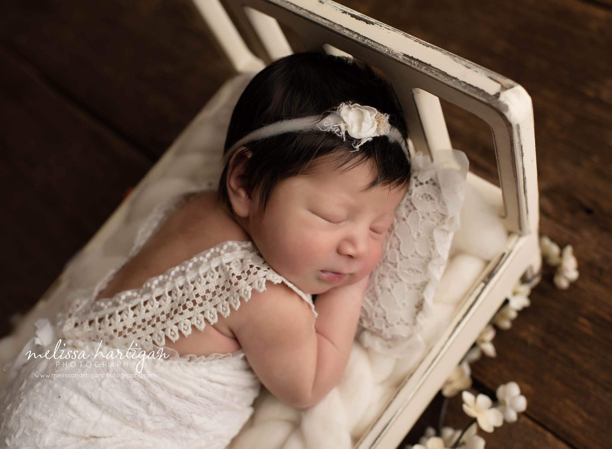 Baby girl laying on tummy on newborn bed wearing white lace romper