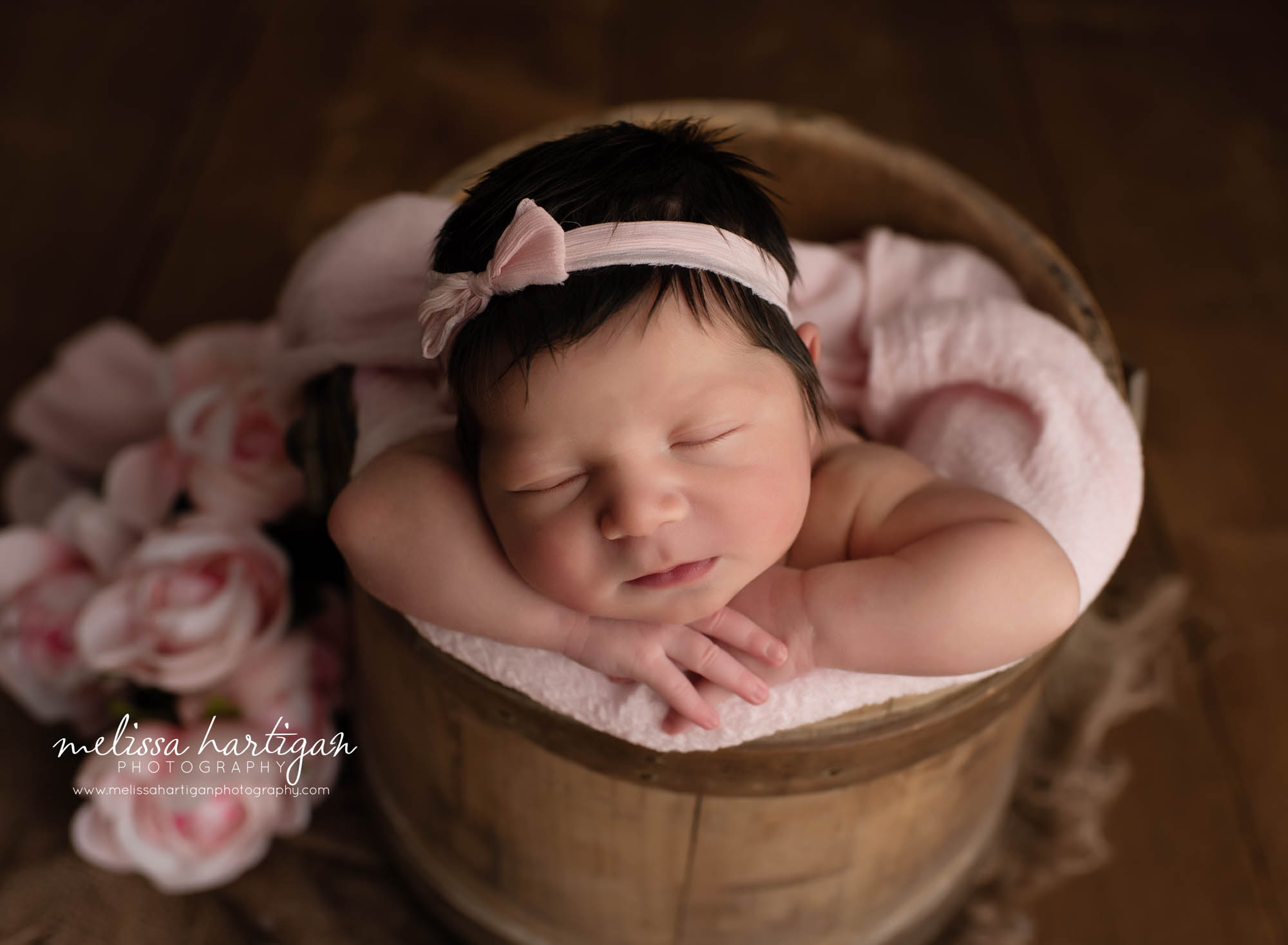 Baby girl with head on hands posed in bucket with pink flowers Waterbury Newborn Photographer