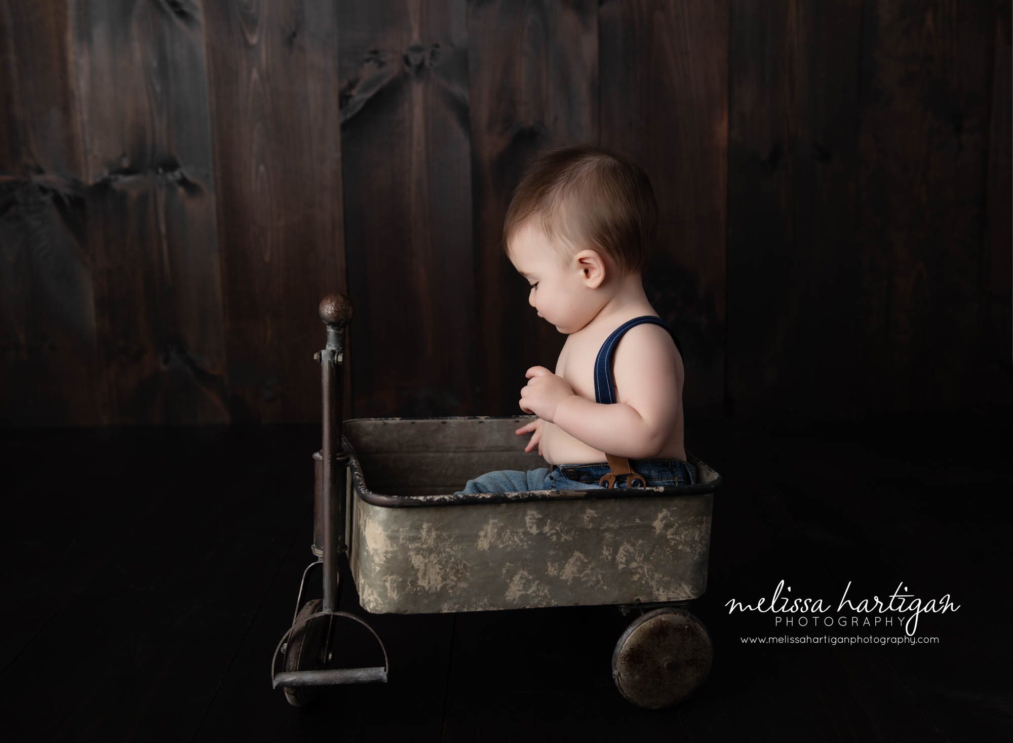 Baby boy sitting in wagon in baby milestone photography session in CT studio