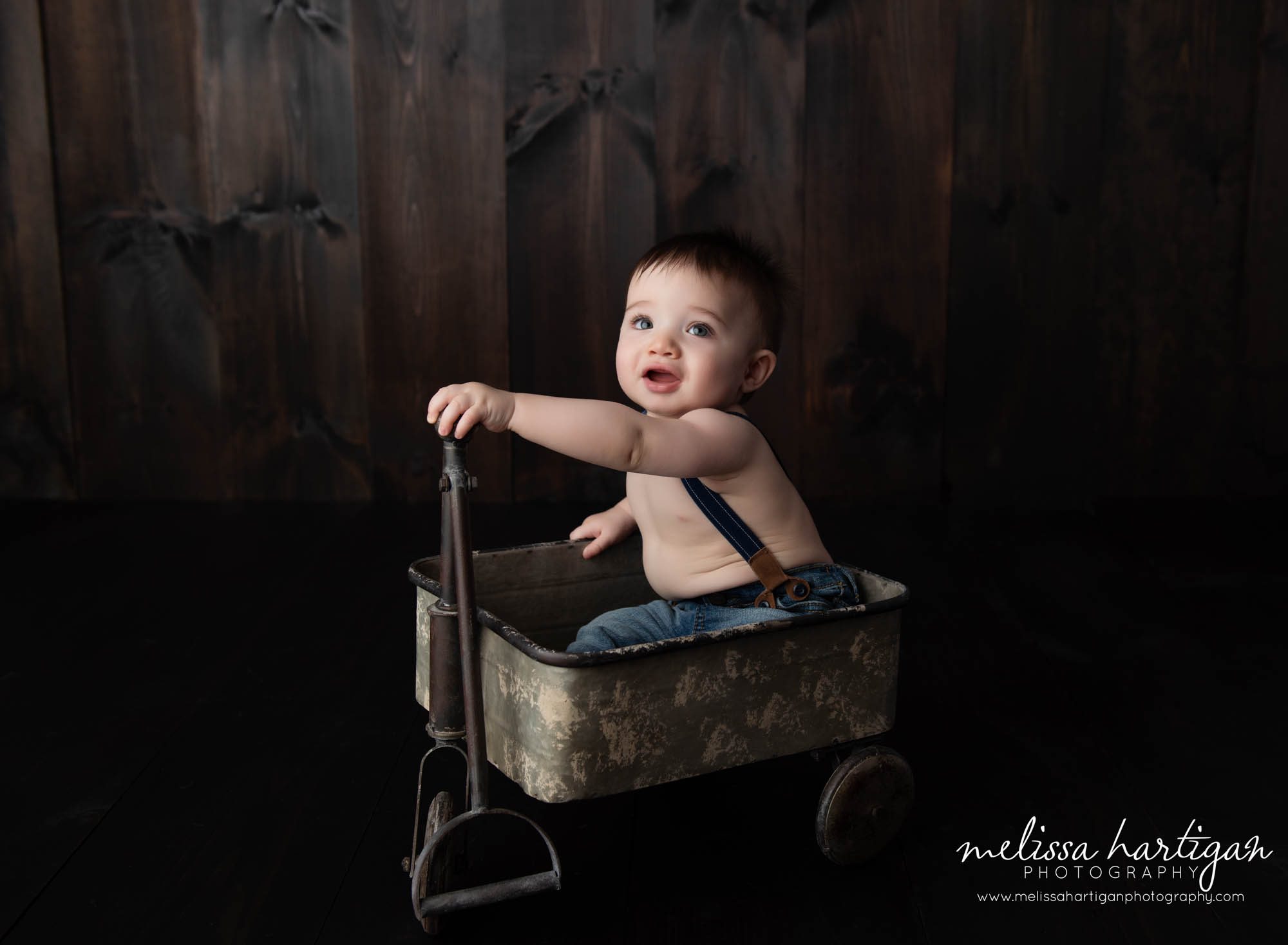 studio baby milestone session capturing baby boy sitting in metal wagon holding