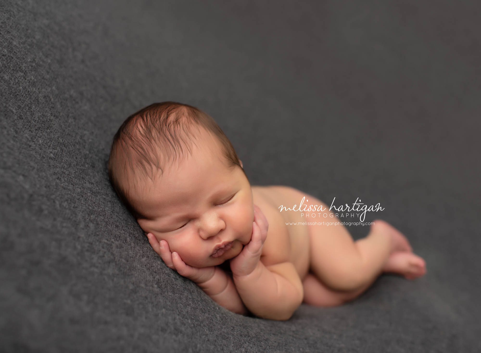 Baby boy posed on grey blanket with hands under chin resting on cheeks Ellington CT Newborn Photography
