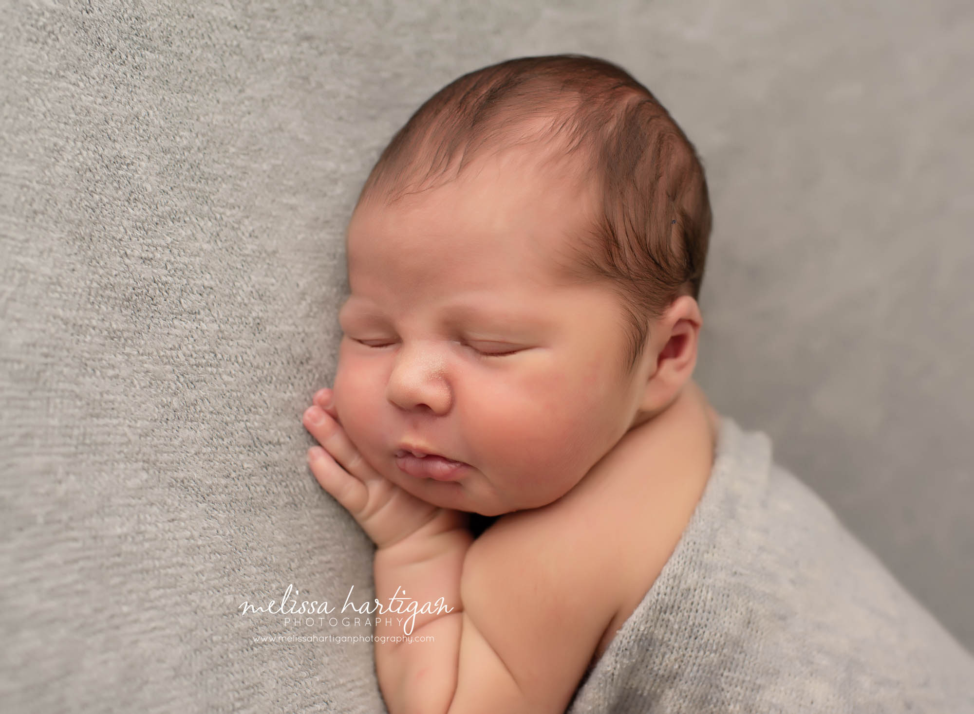 Baby boy resting cheek on his hand lgiht grey blanket posed newborn photography Tolland County CT newborn photographer