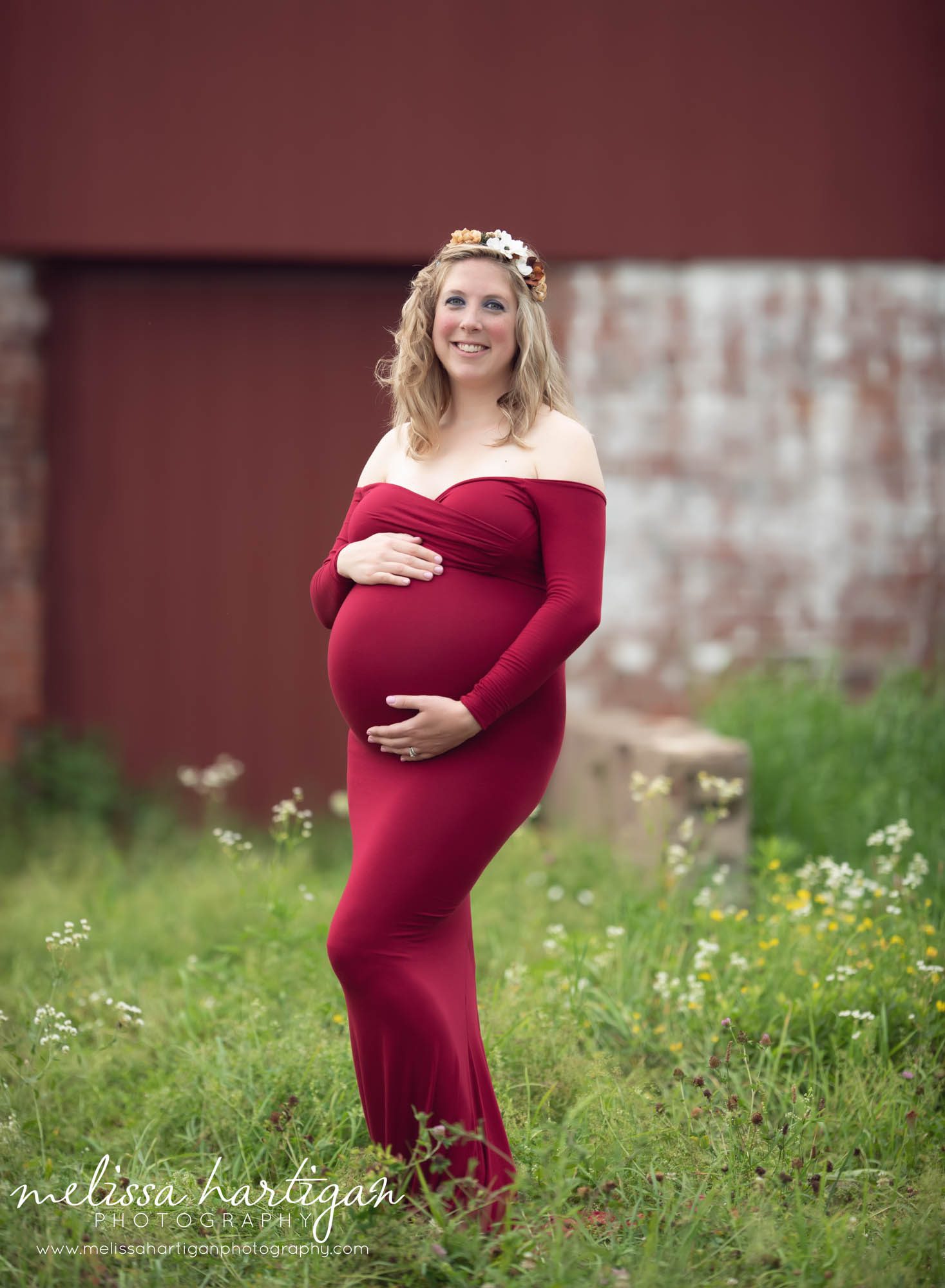 Pregnanct mom standing holding baby bump wearing long fitted red maternity dress off the shoulder Maternity photographer CT