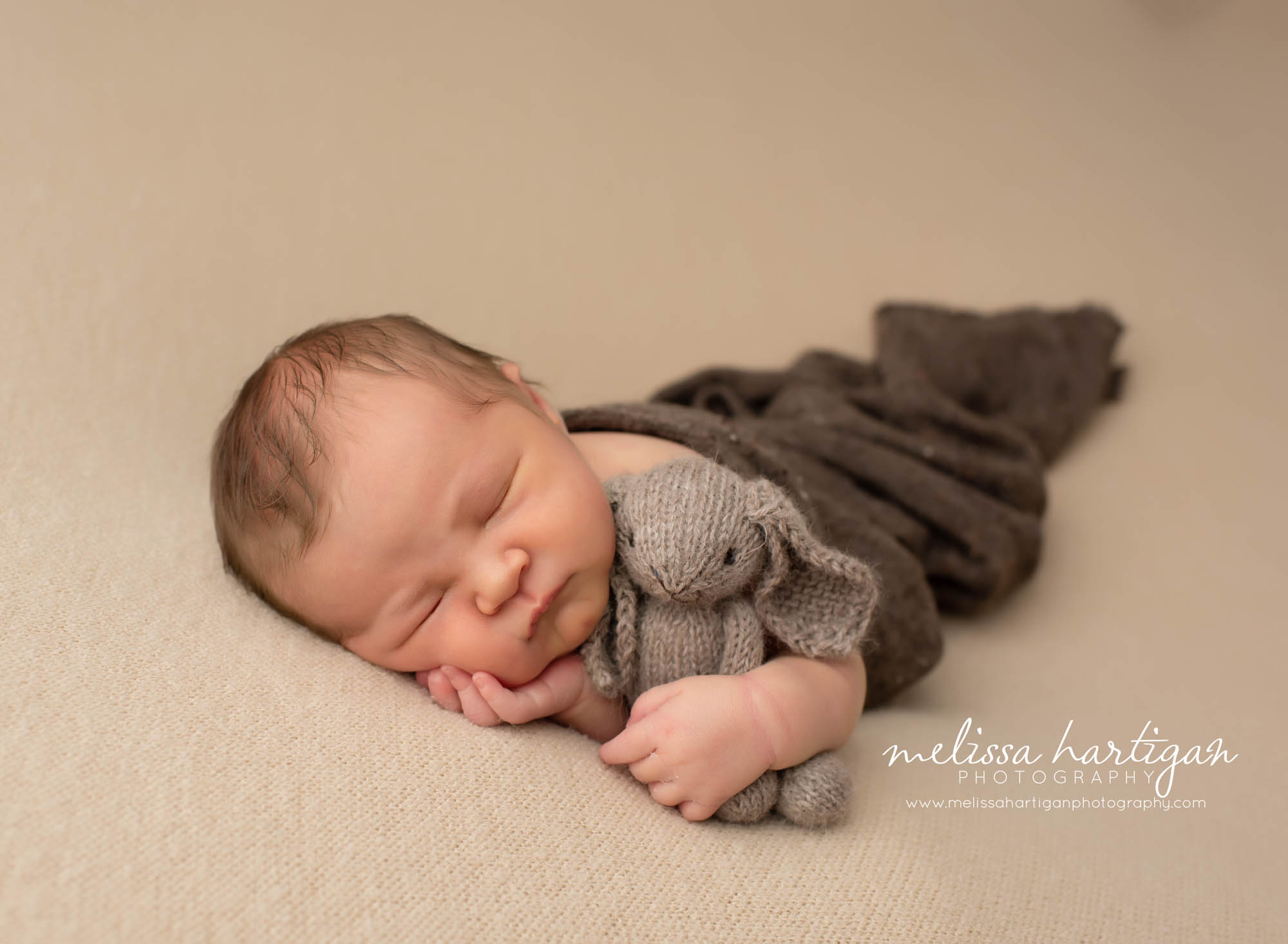 Baby boy posed on neutral color blanket backdrop with knitted bunny