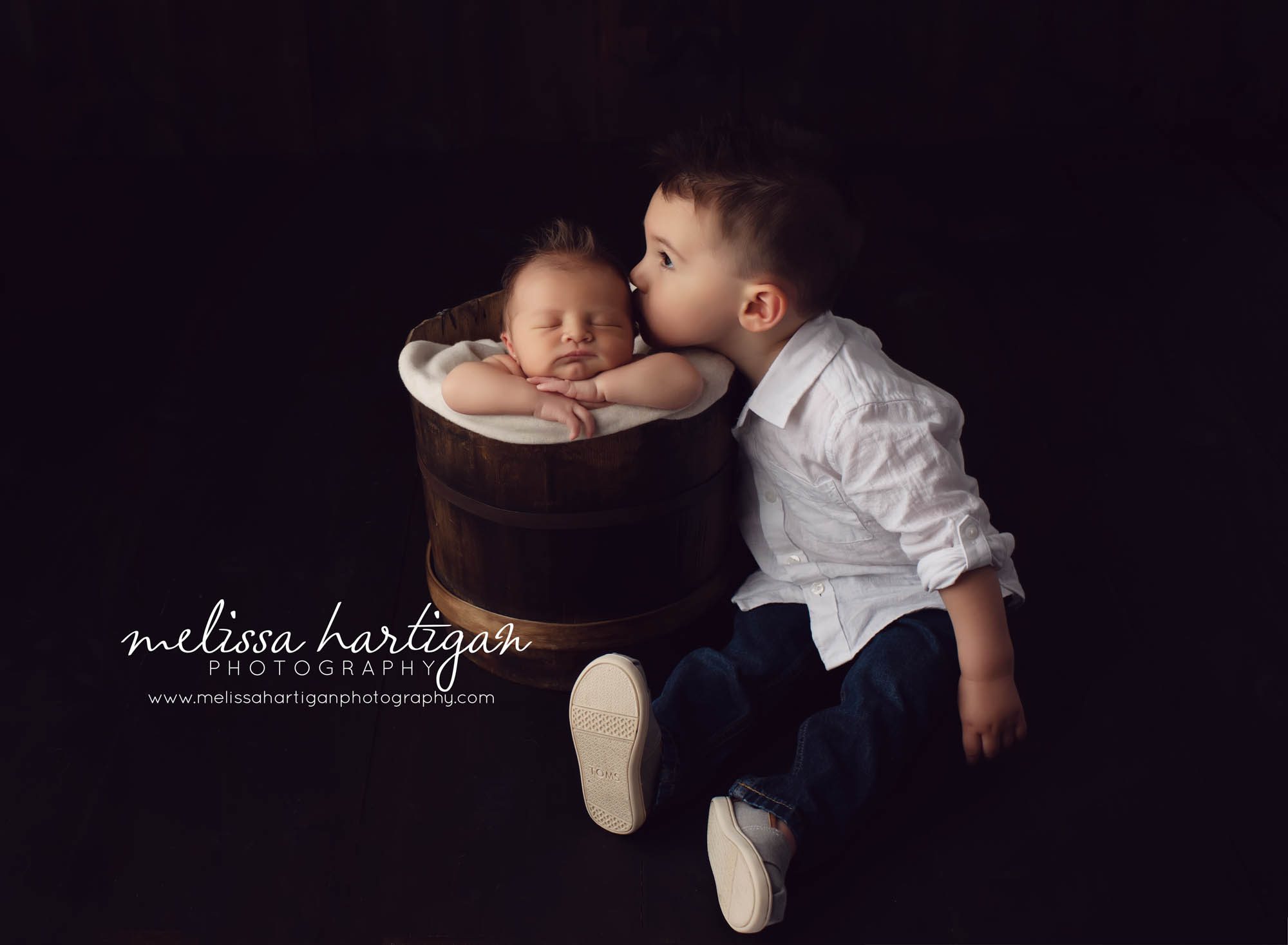 toddler boy kissing newborn baby brother posed in bucket