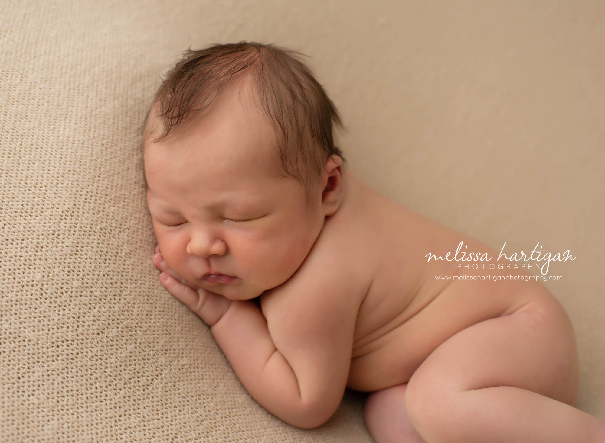 baby boy posed side laying on neutral colored blanket backdro