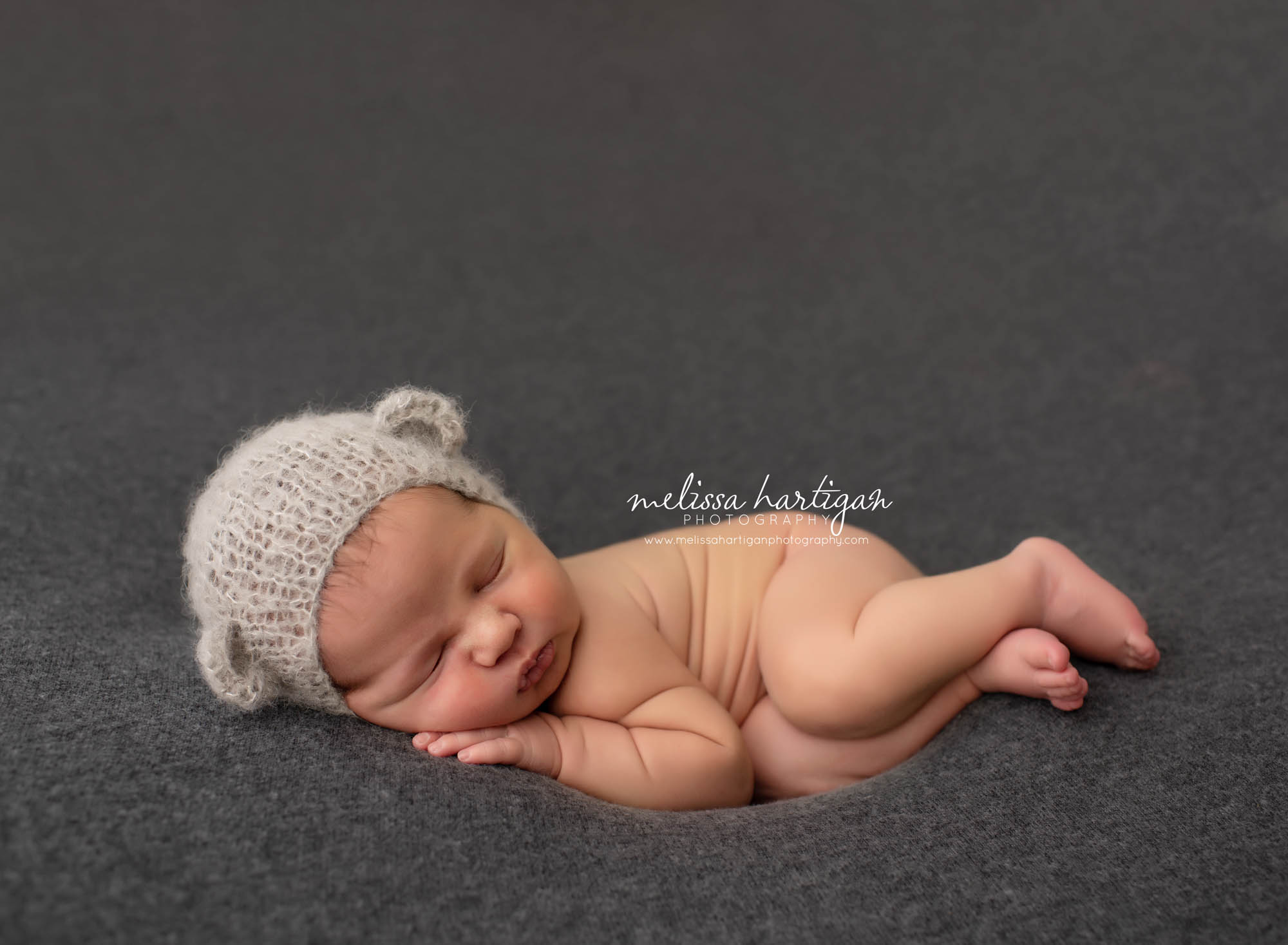 baby boy sleeping on side with light grey knitted bear bonnet