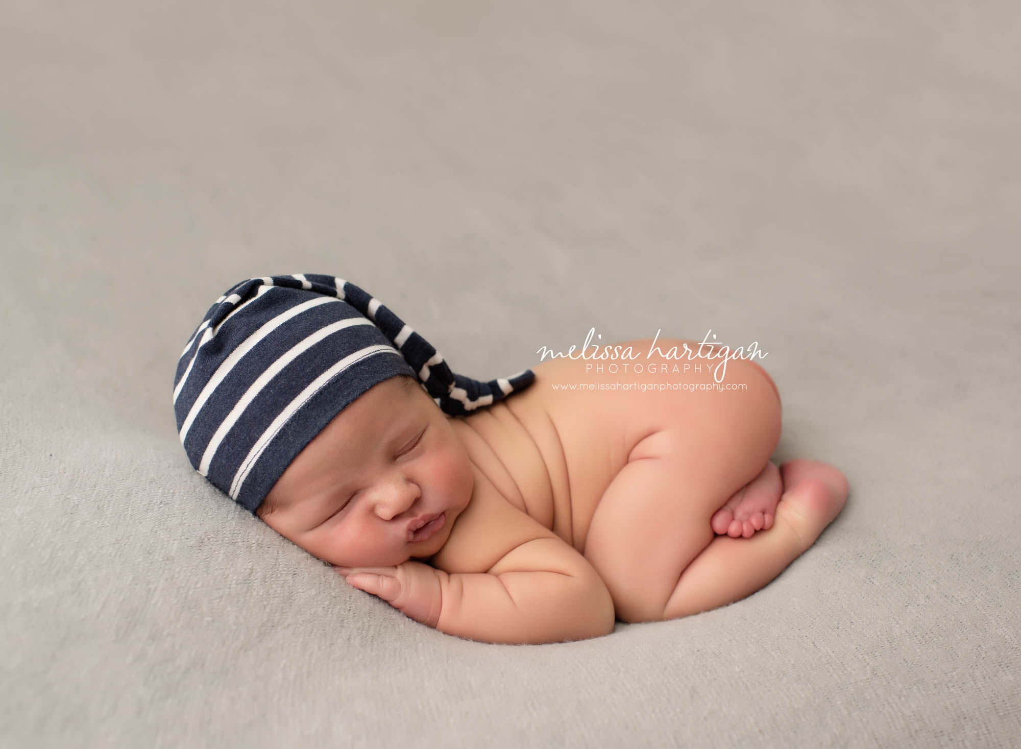 newborn baby posed bum up pose newborn photography studio session baby wearing navy blue and white striped sleepy cap hat