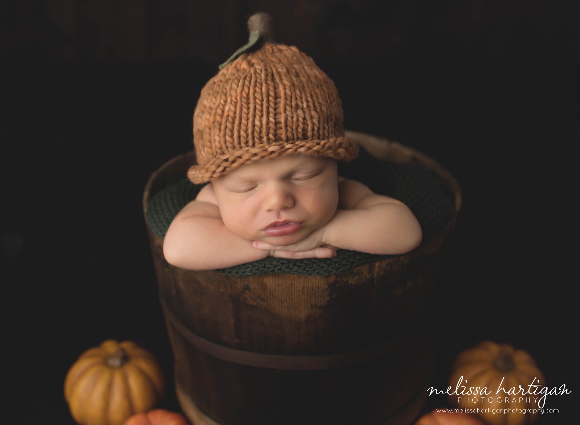 Newborn baby boy posed in bucket wearing knitted fall pumpkin hat Experienced CT newborn Photographer