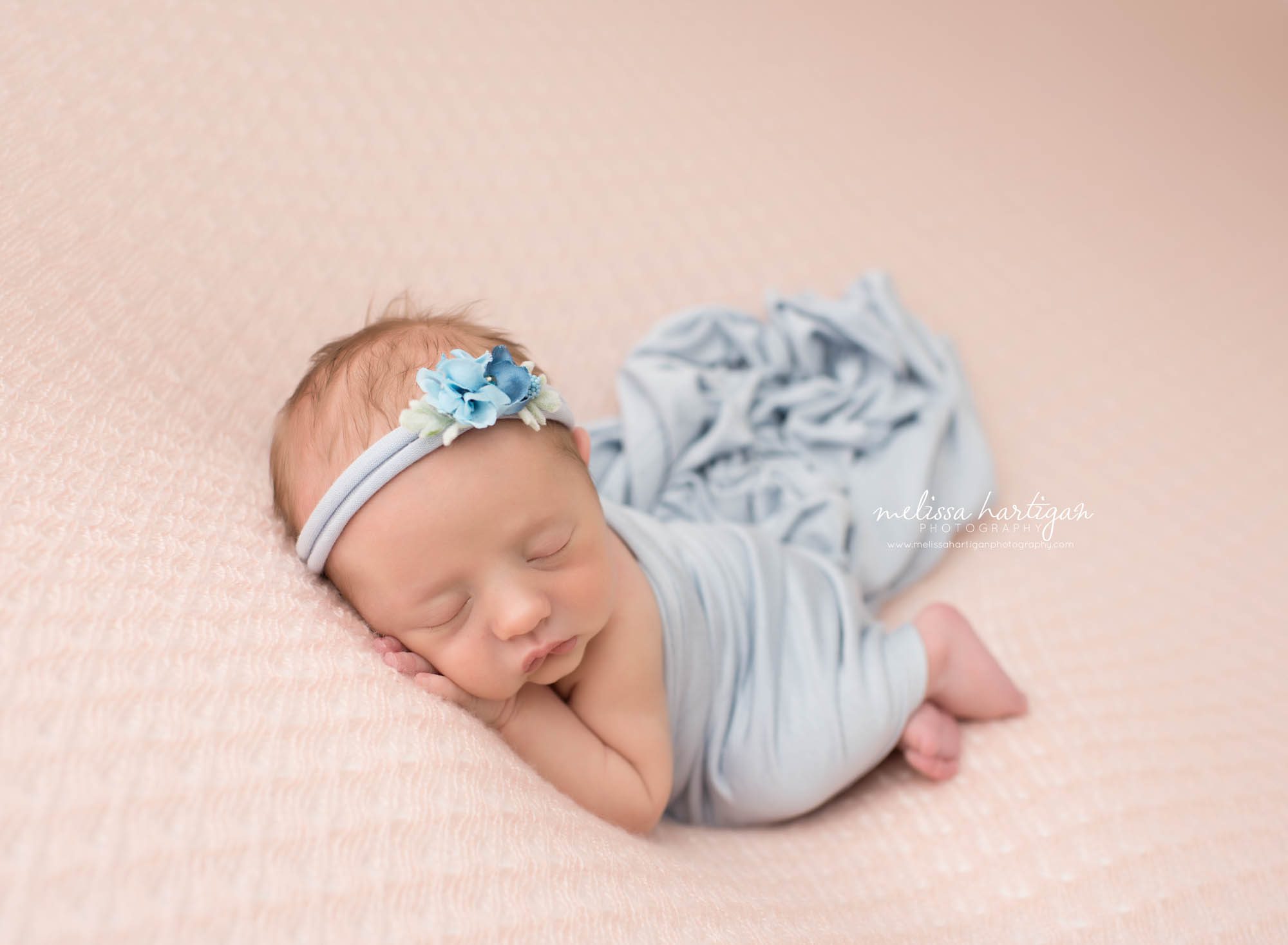 Baby girl posed laying on her side with blue wrap and blue flower headband Lebanon CT newborn Photographers