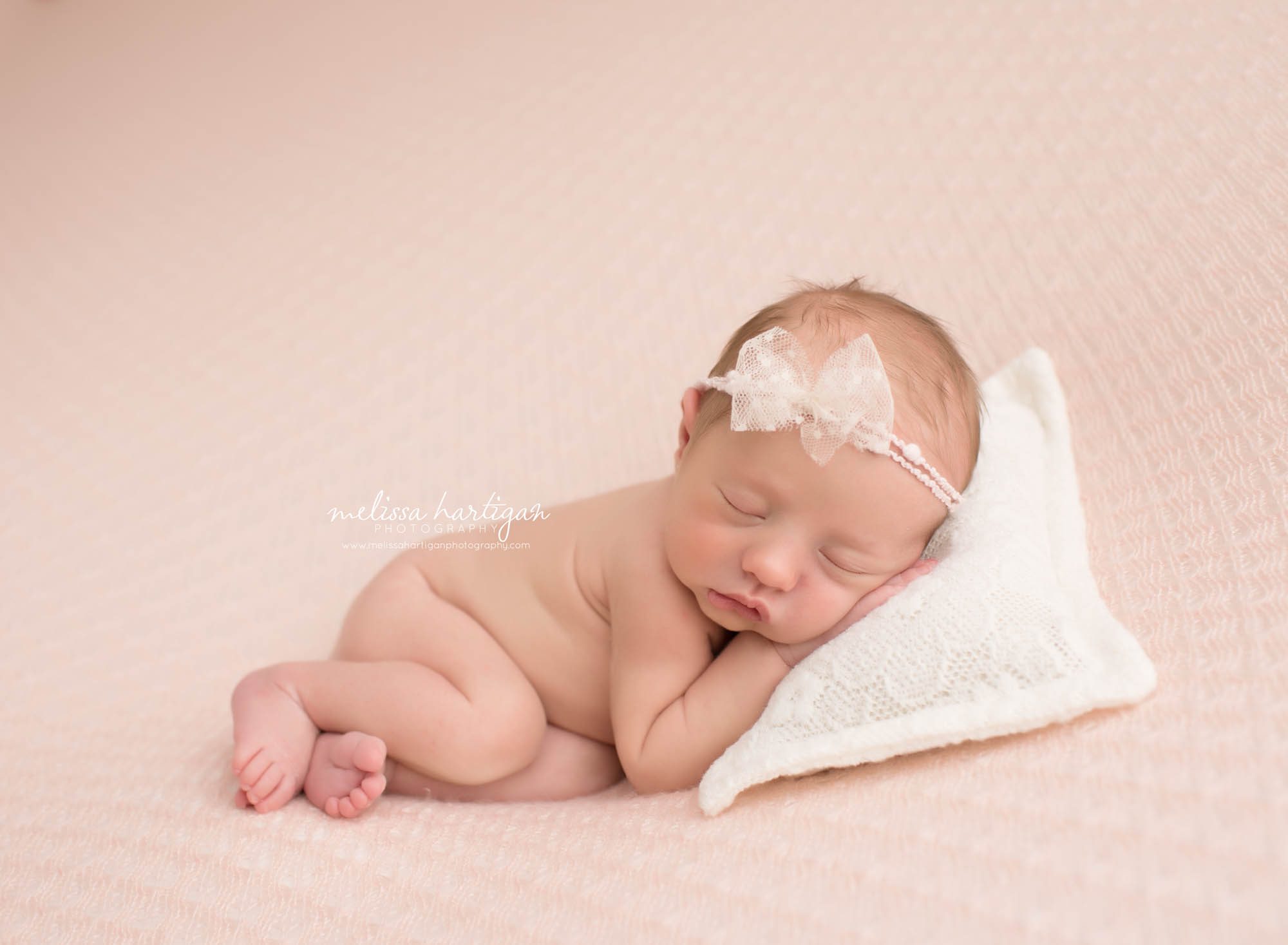 Baby girl posed on textured blanket with bow headband sleeping on newborn pillow