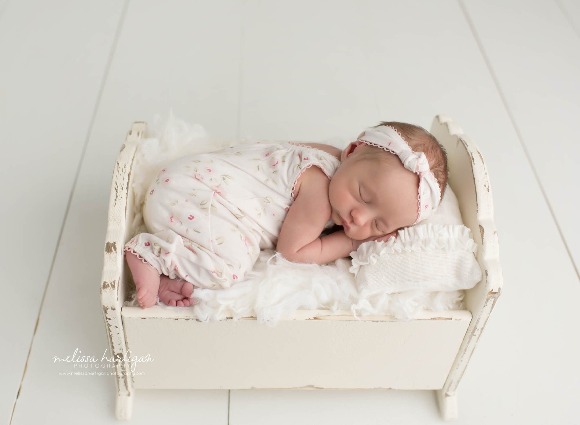 Baby girl posed in cradle prop wearing floral newborn outfit and headband CT baby photography