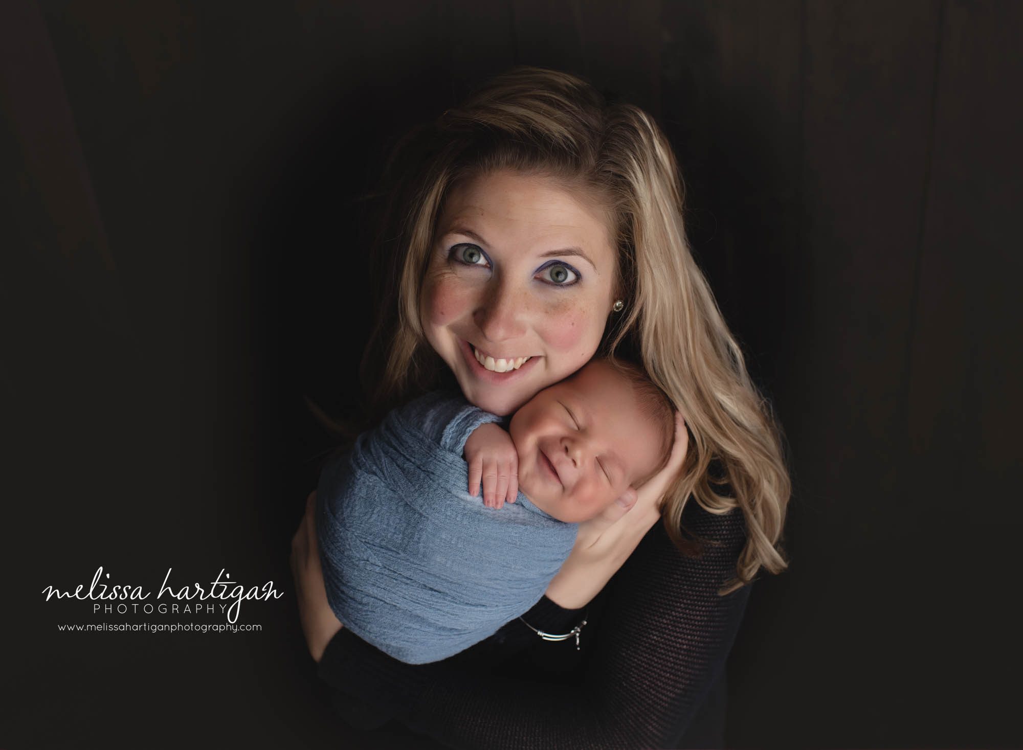 baby boy smiling and wrapped in blue while mom holds him parent pose studio newborn and family photographer CT Columbia