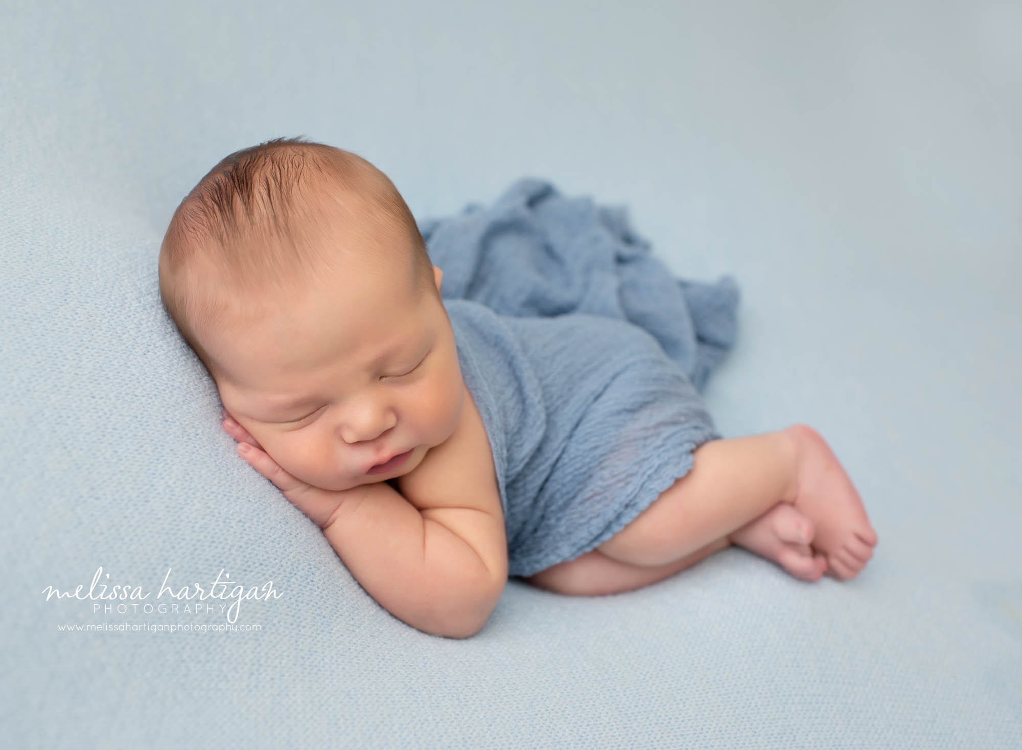 Newborn boy sleeping on side with blue wrap on light blue backdrop