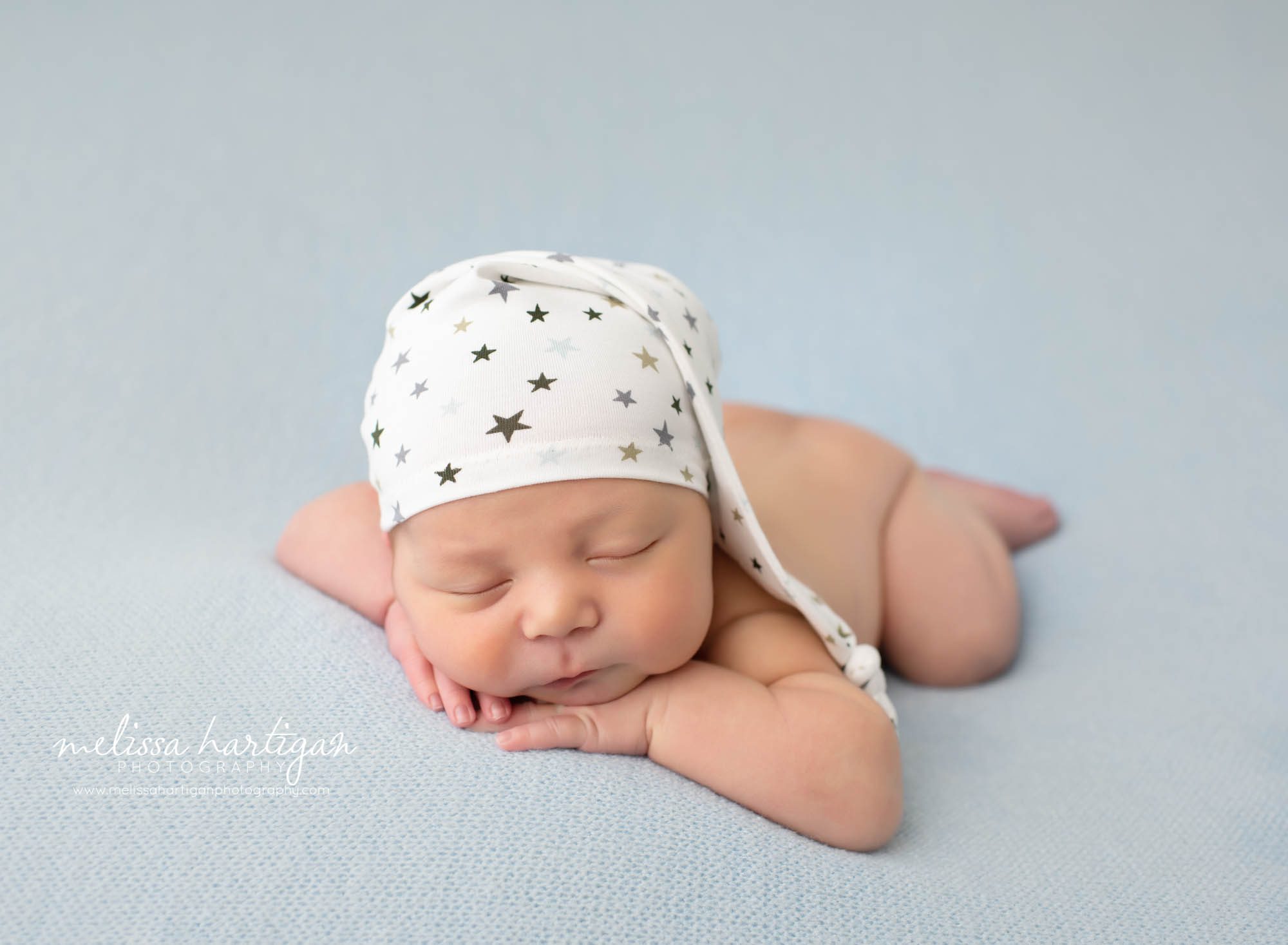 baby boy posed on light blue textured blanket with white and grey and blue sleepy hat with stars