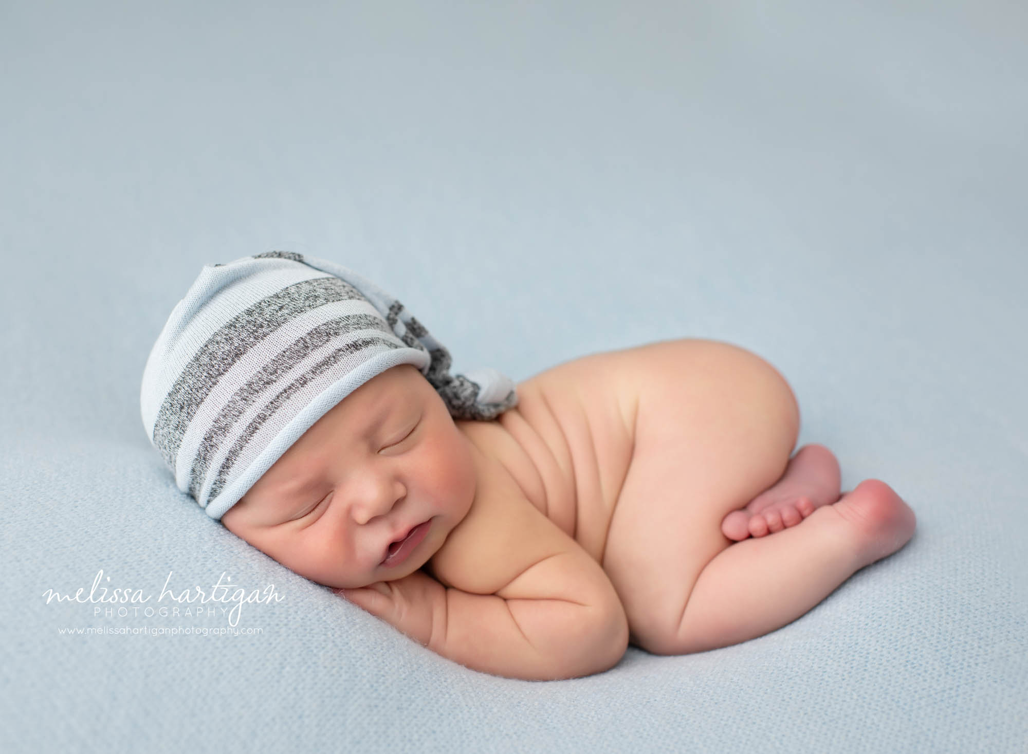 Baby boy posed on light blue backdrop with light blue and grey sleepy cap on