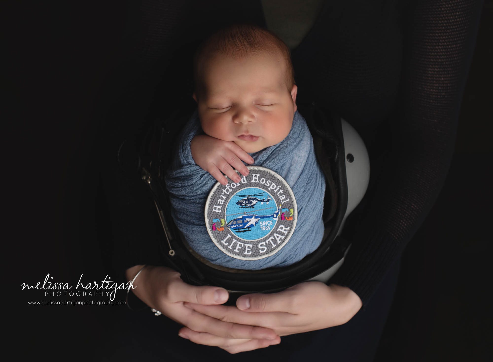 newborn baby boy wrapped in blue sitting in helmet with Hartford Hospital Lifestar flight badge Columbia CT baby photographer