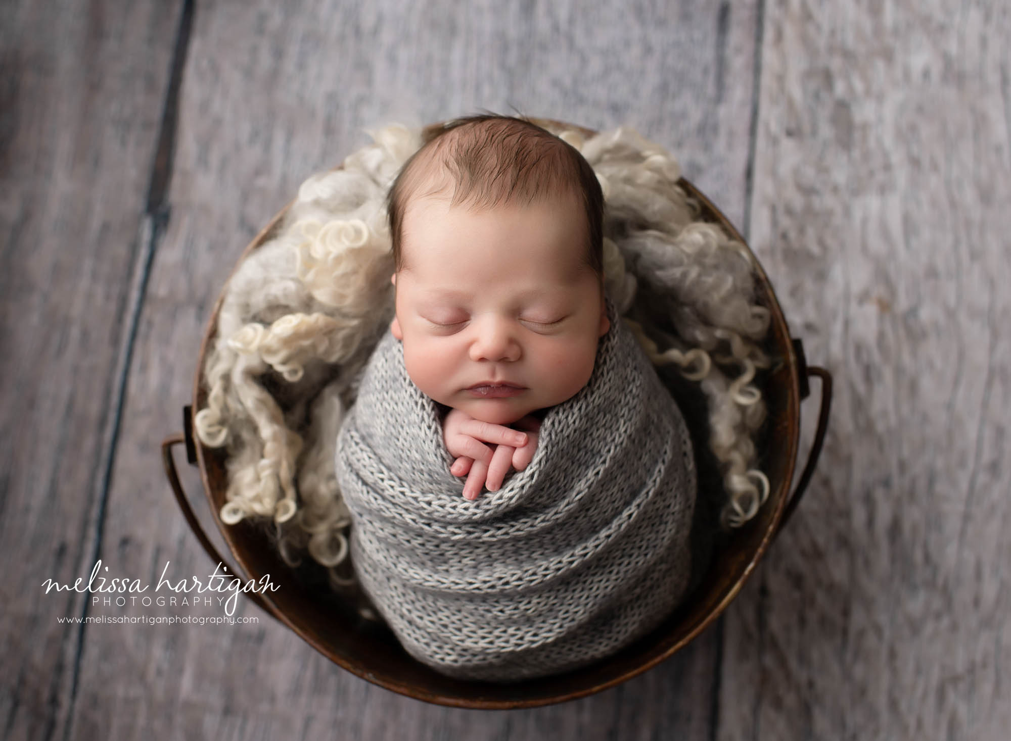 Baby boy wrapped in knitted grey wrap with neutral colored curly layers