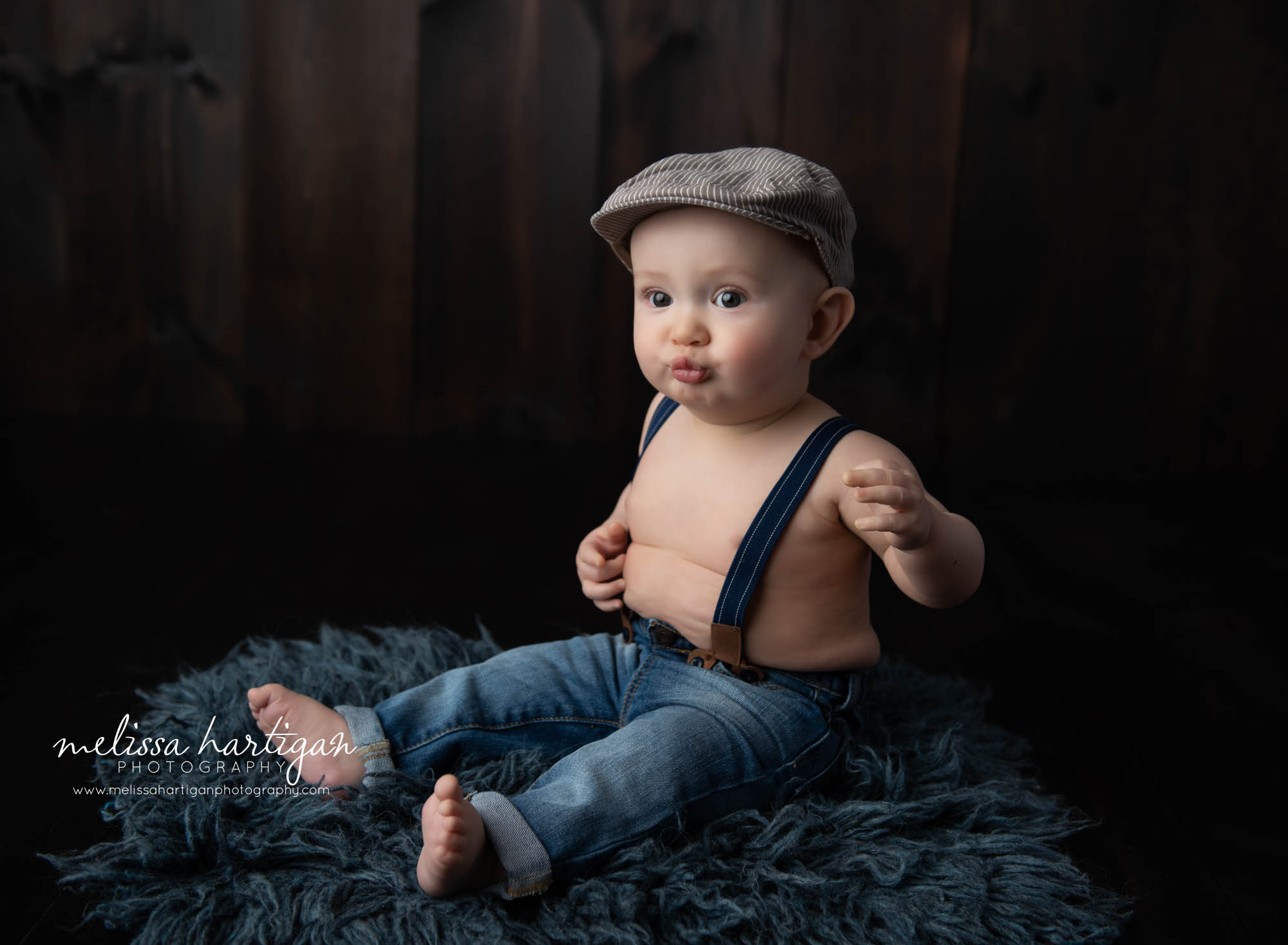 baby boy sitting on blue flokati with jeans and suspenders on