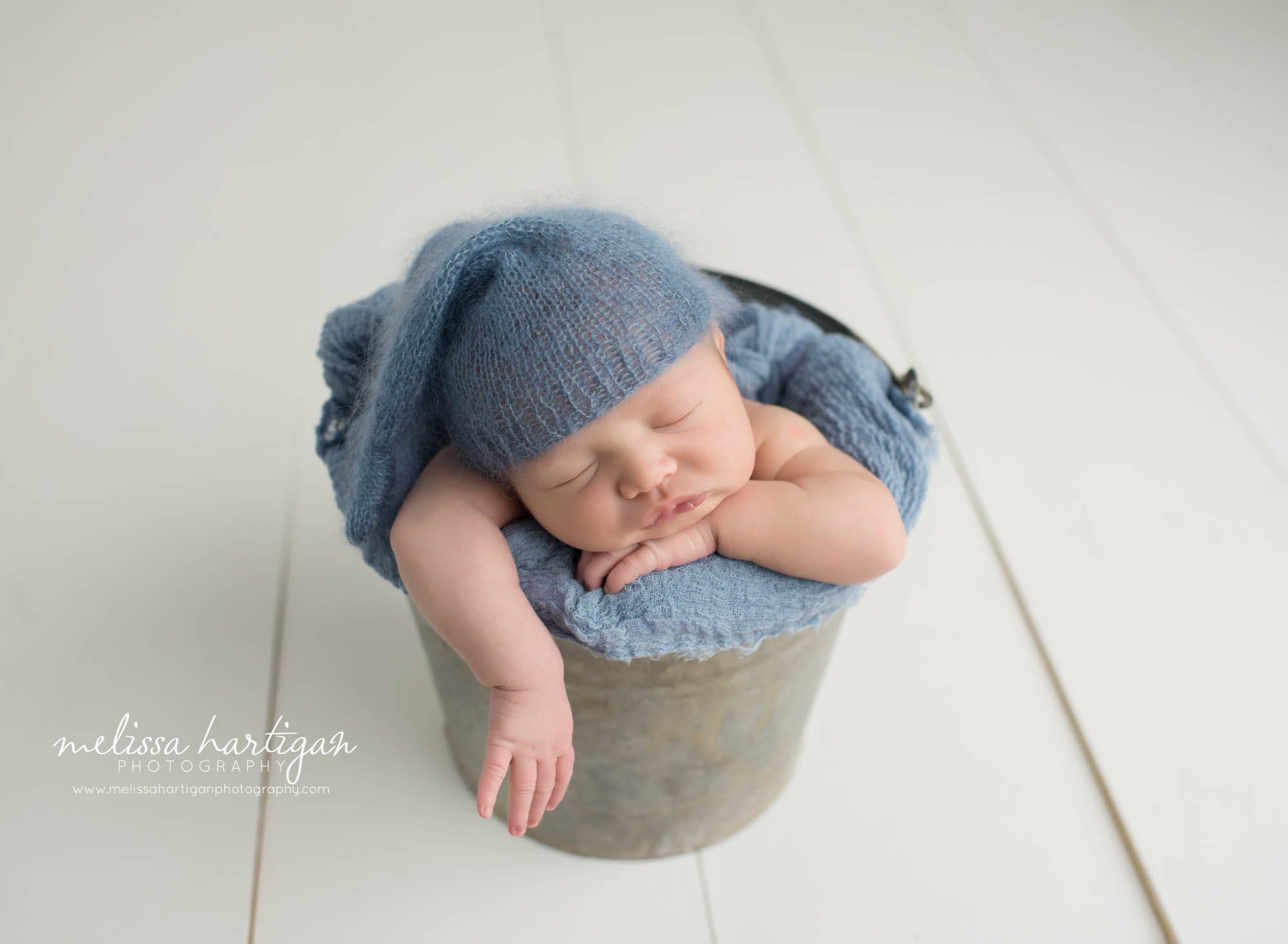 Baby boy posed in metal bucket wearing knitted blue sleepy cap