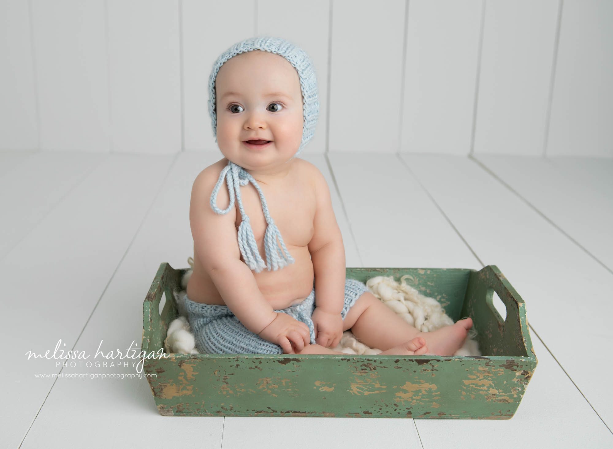 baby boy sitting in wooden tray wearing light blue matching knitted hat and short set