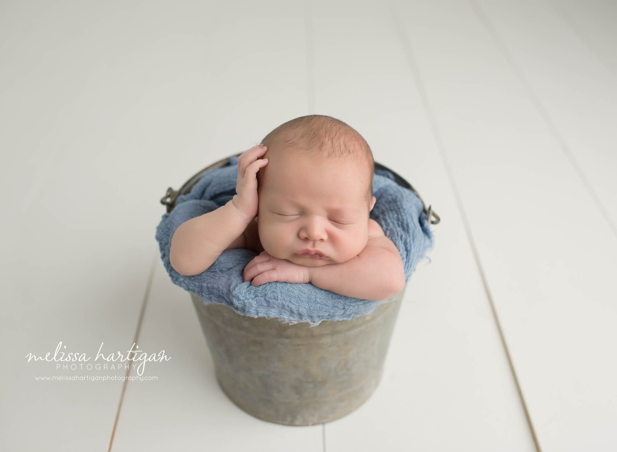 Baby boy posed in metal bucket with hand on the side of his head
