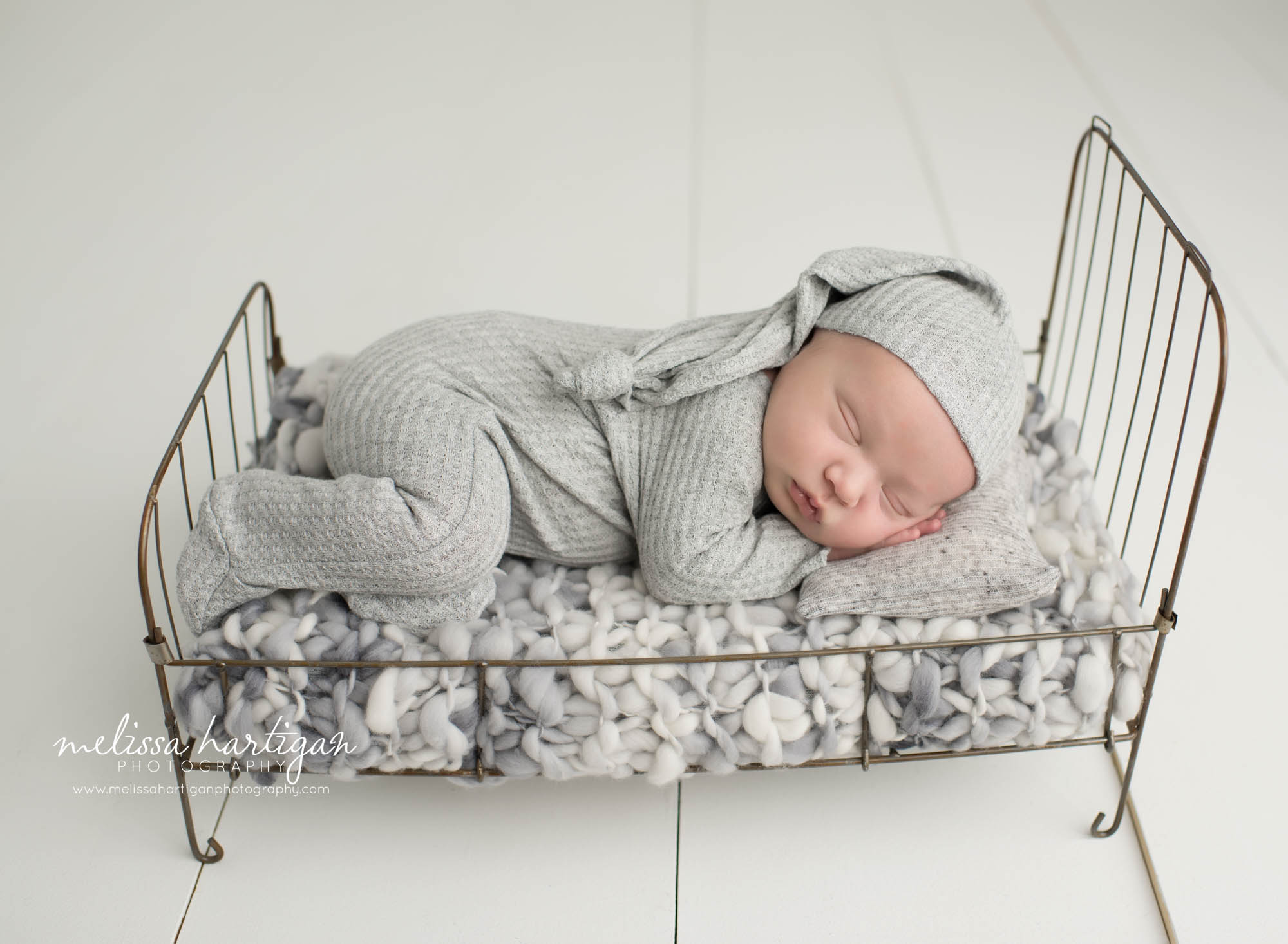 Baby boy posed on metal bed with grey knitted layer and grey outfit and hat set