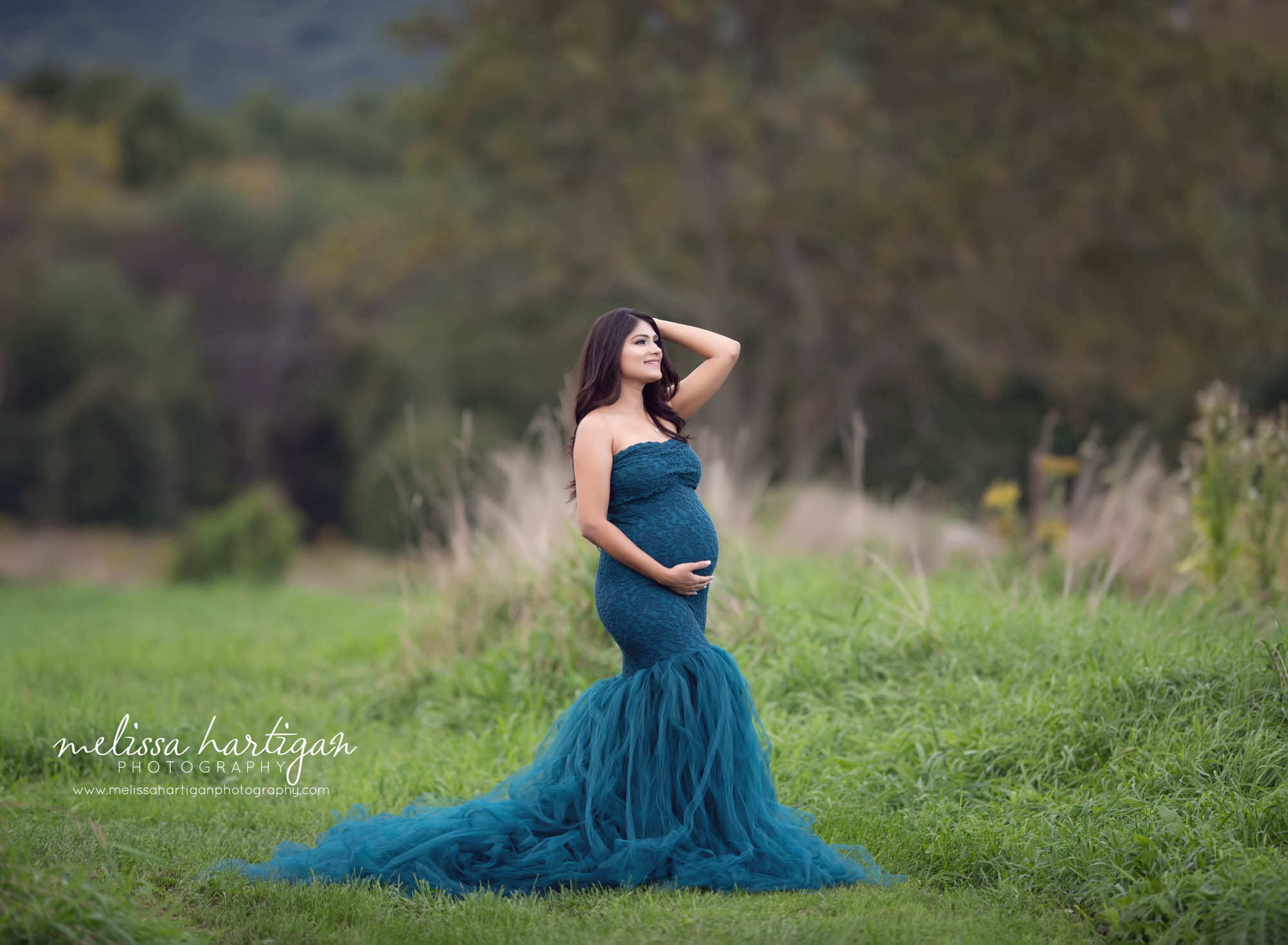 expectant mom standing maternity pose holding baby bump wearing dark teal lace maternity dress gown