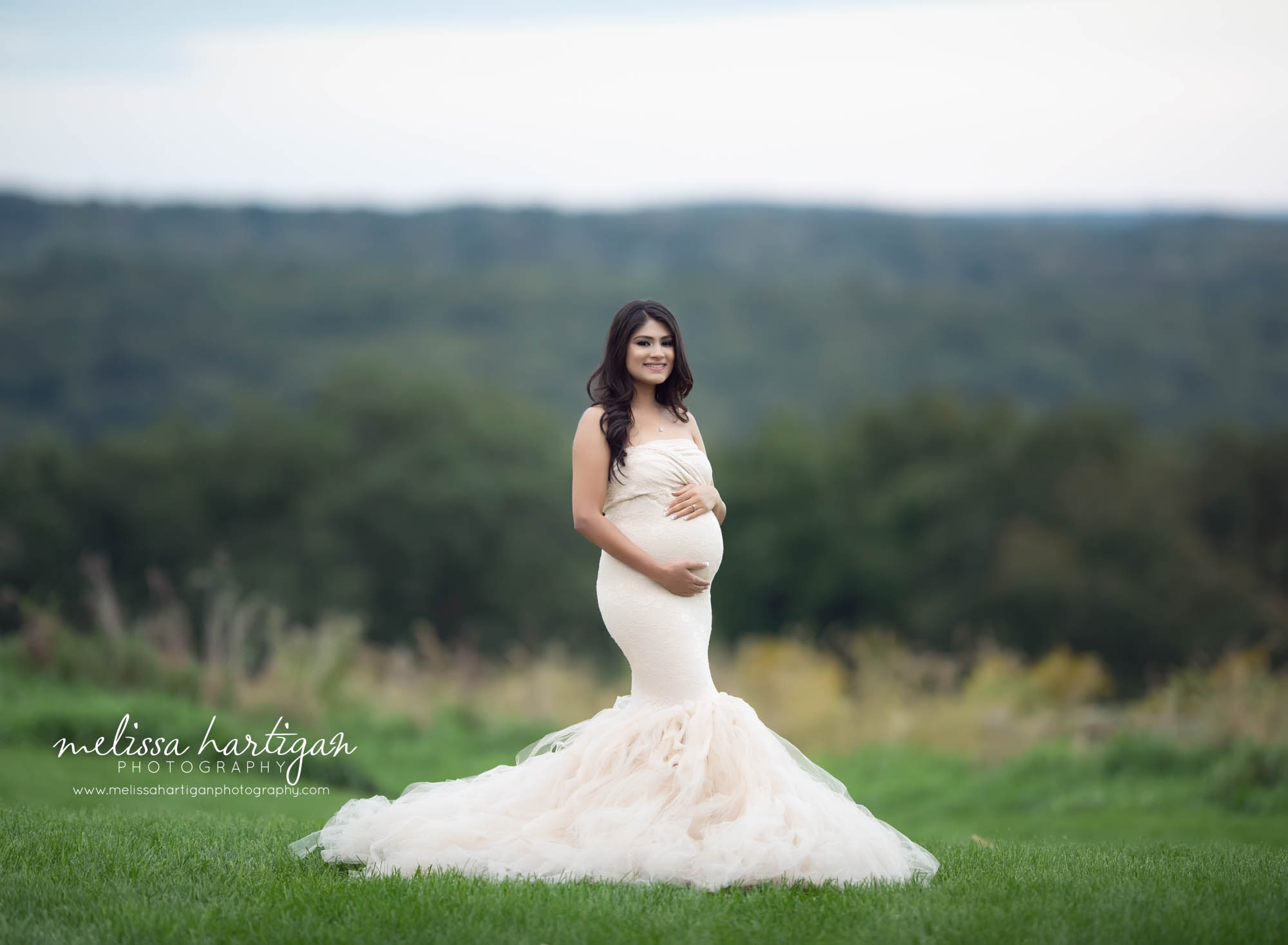 expectant mom holding her pregnant baby bump wearing fitted long mermaid style maternity gown