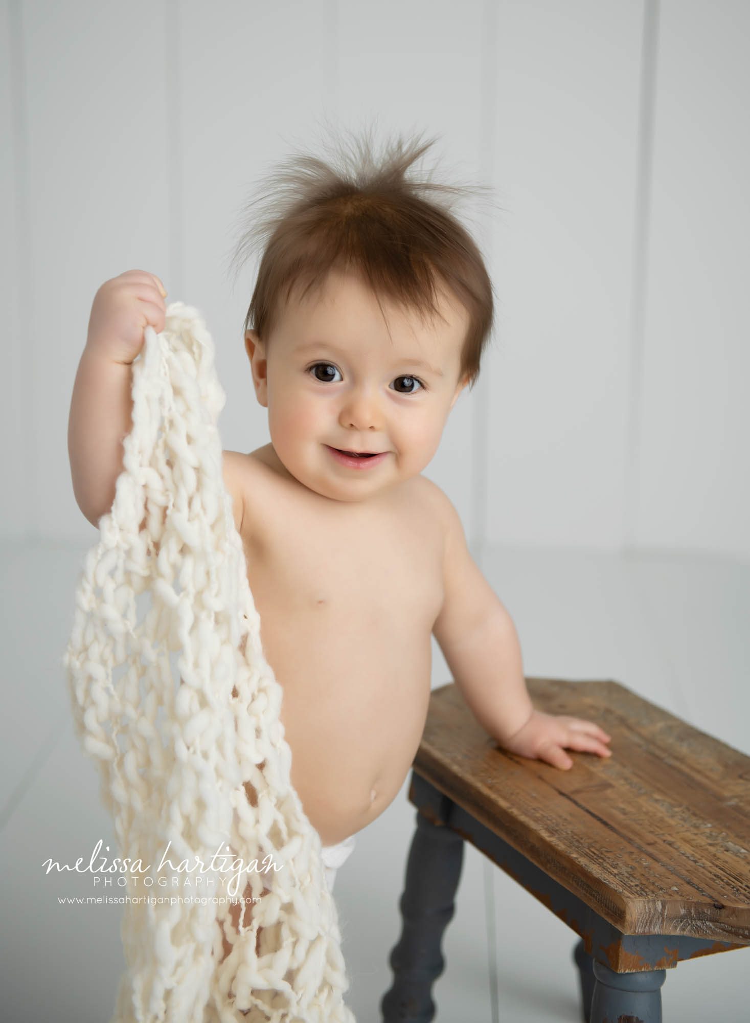 baby girl standing up holding cream knitted blanket