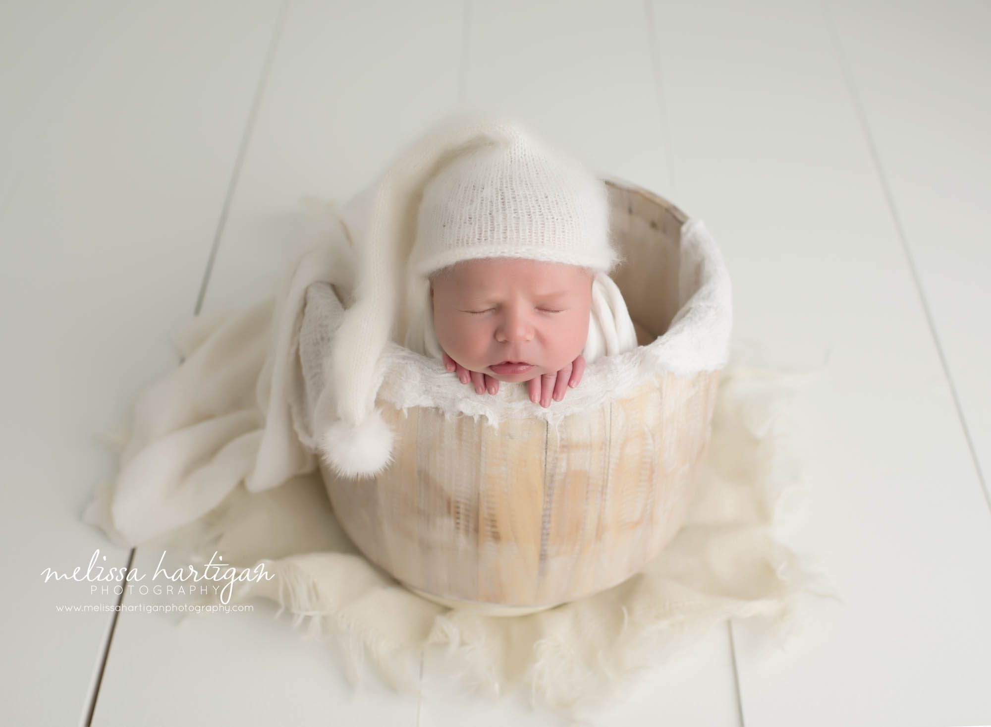 Baby boy posed in bucket with cream and white knitted sleepy cap