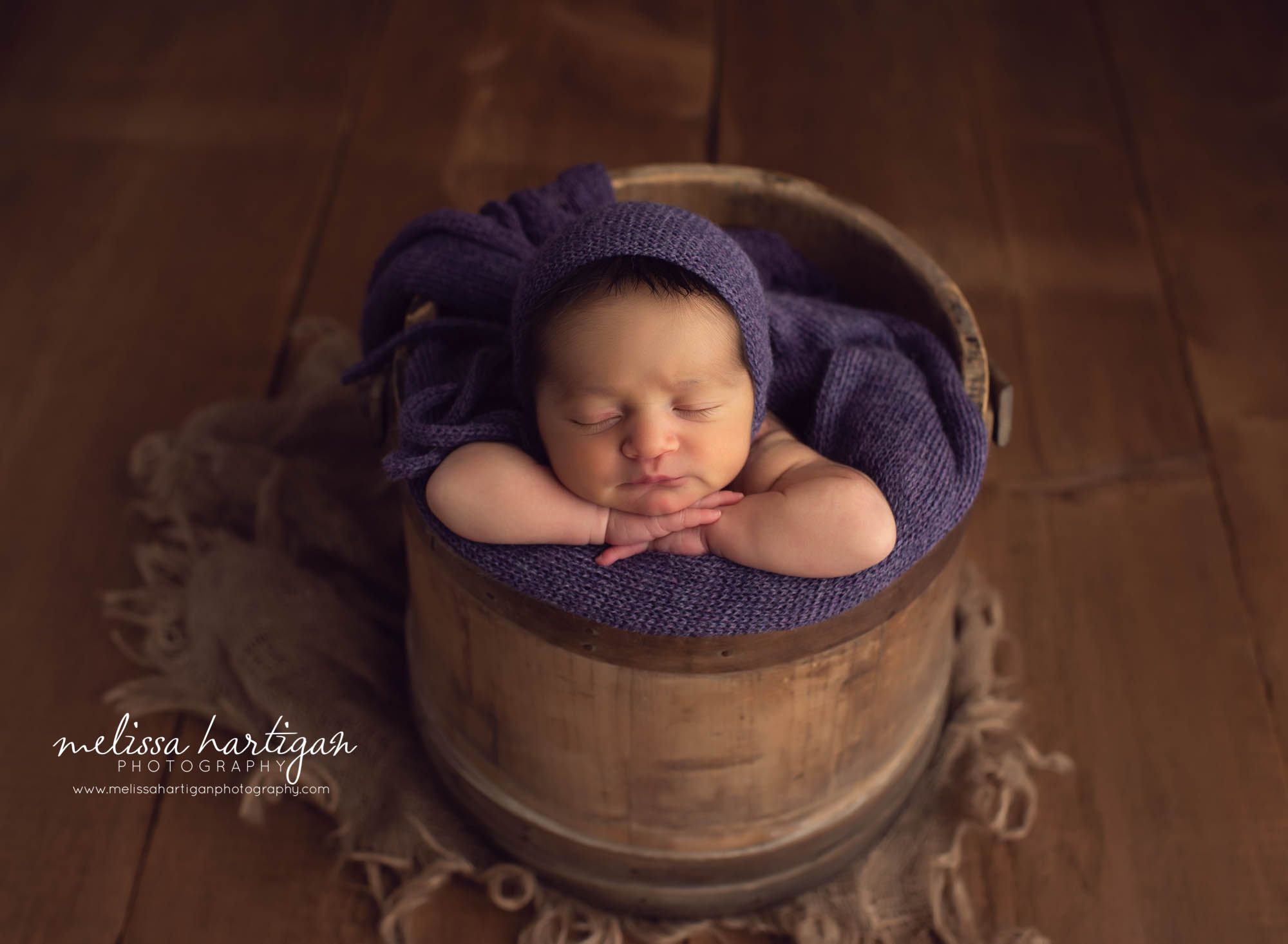 Baby girl posed in rustic bucket with purple knitted bonnet and purple wrap Ct newborn Photographer