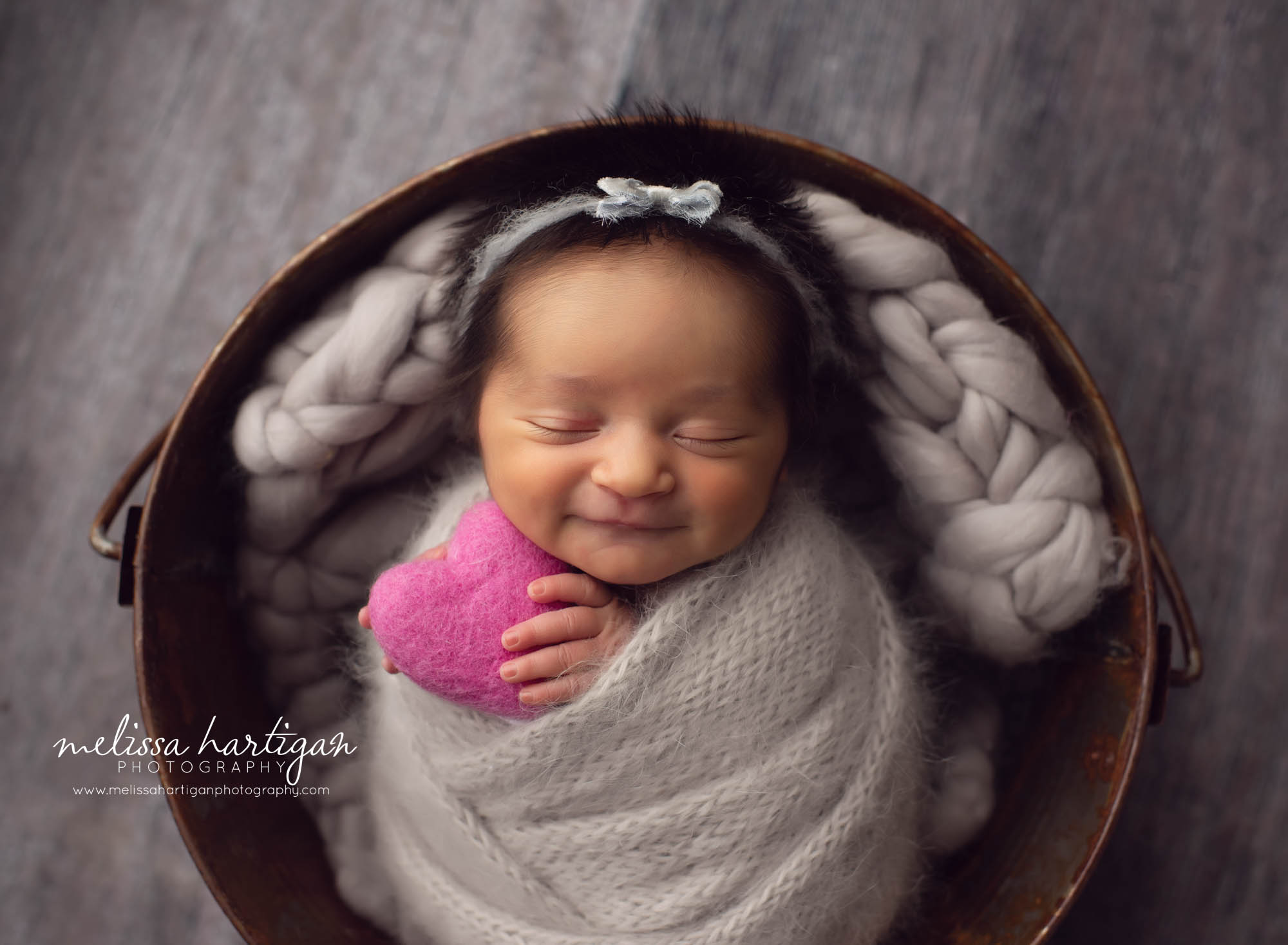Baby girl in metal bucket wrapped up in grey knitted wrap with felted purple heart