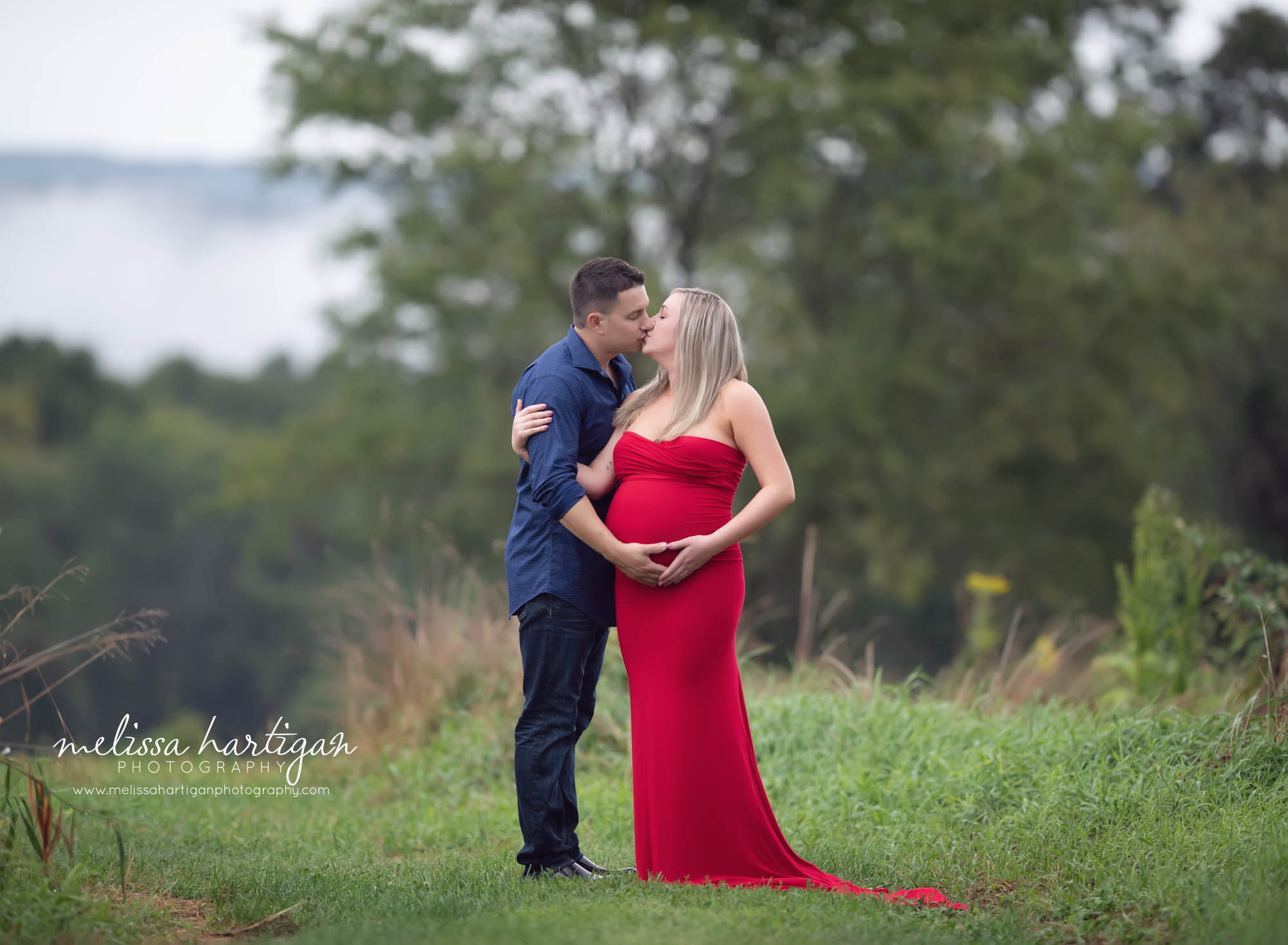 expectant couple kissing holding baby bump mom wearing long fitted red dress