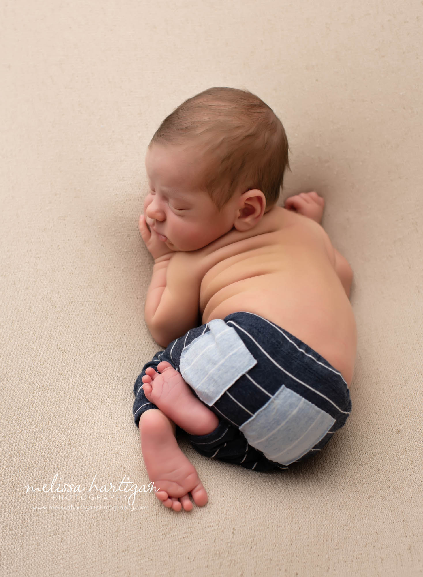 baby posed on tummy with back and bottom up wearing navy blue stripped pants