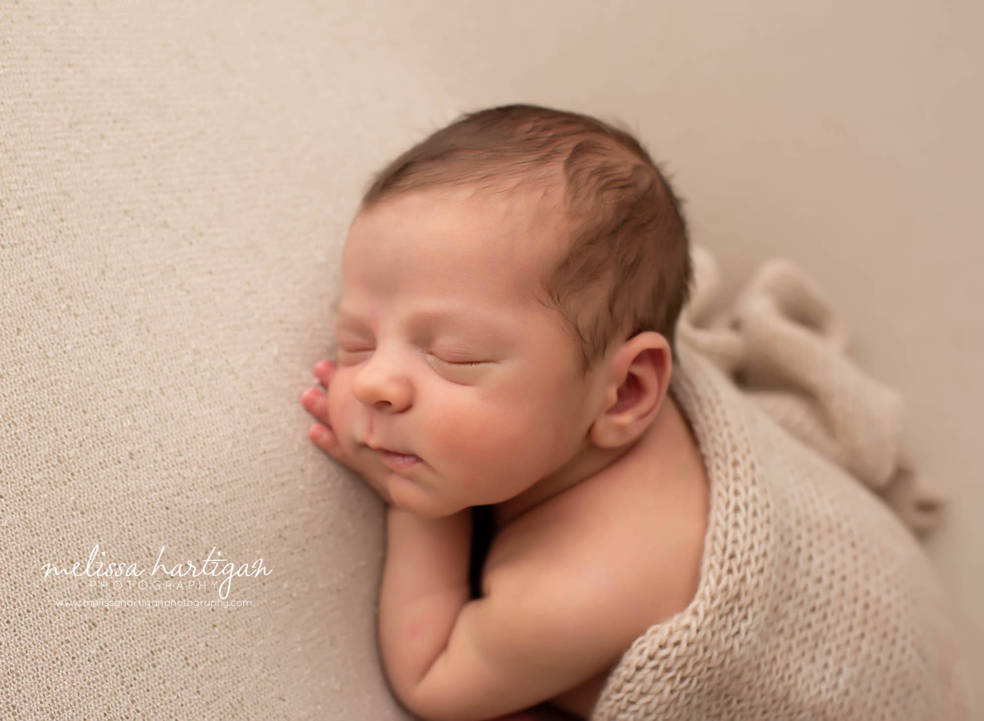 Baby boy posed with hand under cheek on light tan colored wrap and backdrop Connecticut newborn photography