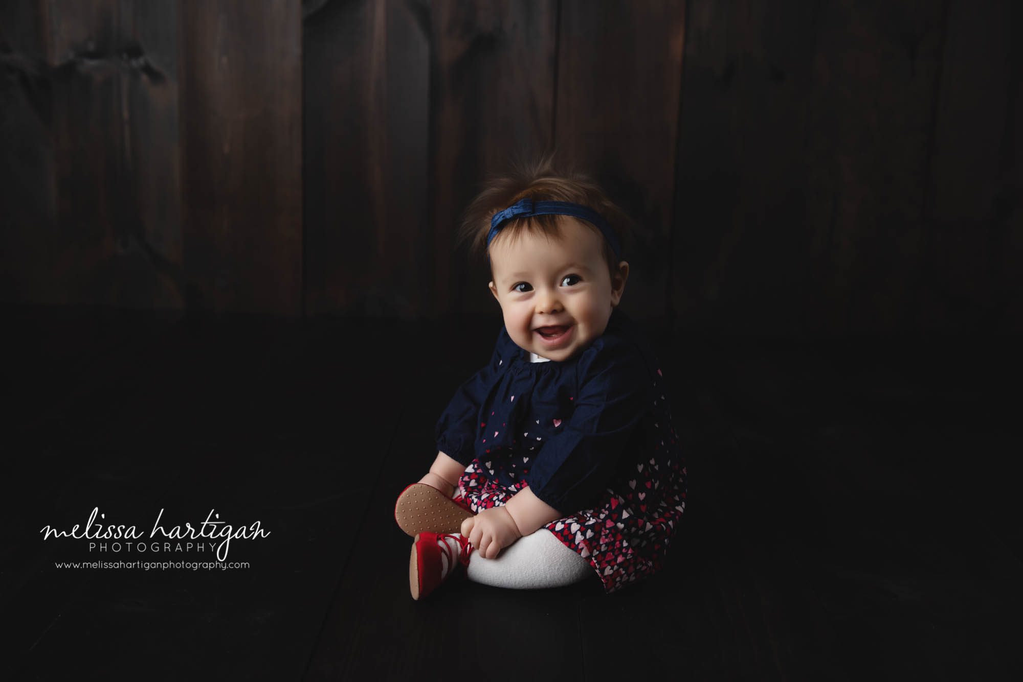 baby girl sitting on dark wooden boards studio baby milestone CT photography session