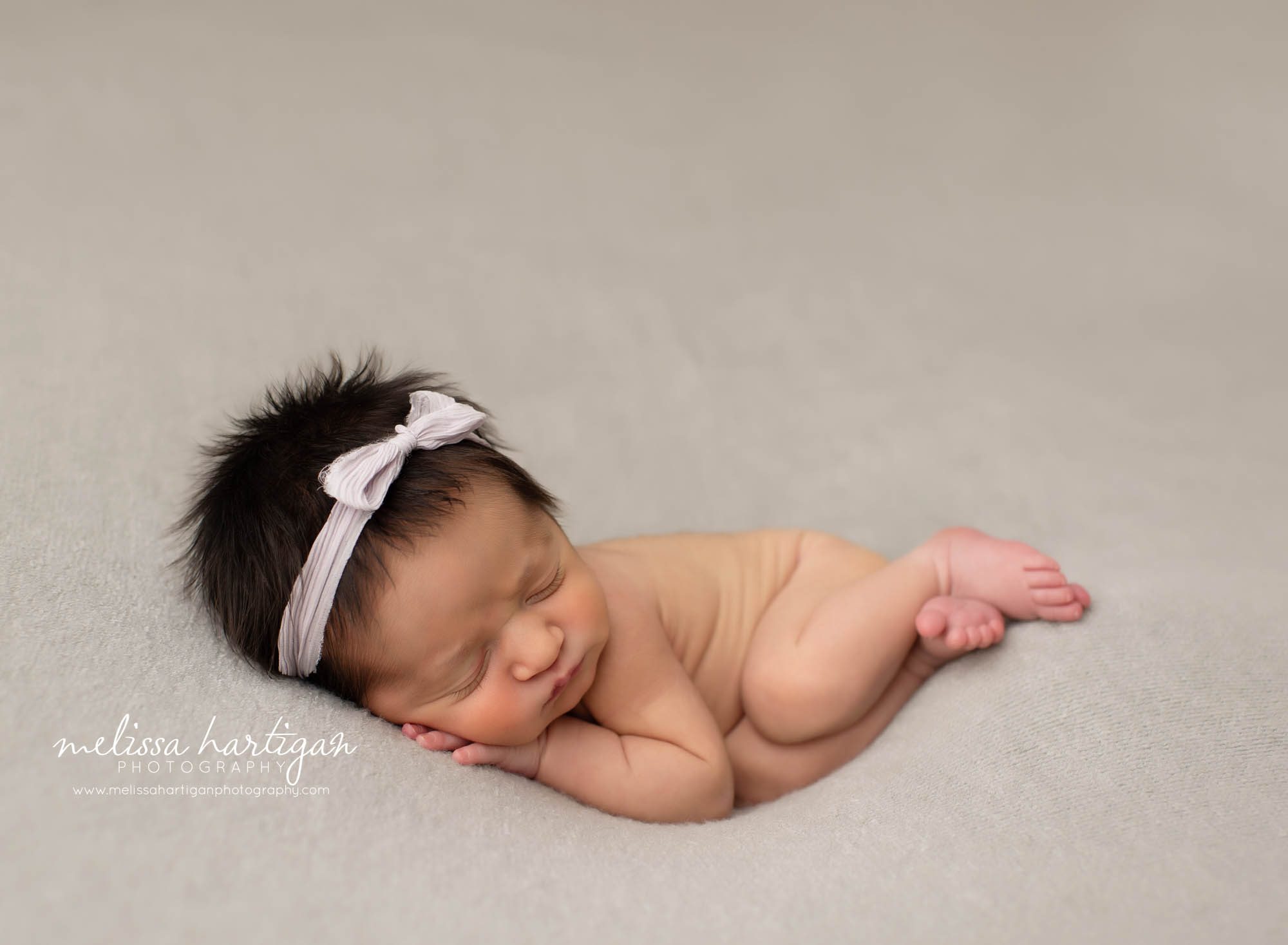 baby girl pose don side with silber bow in hair layng on gray blanket