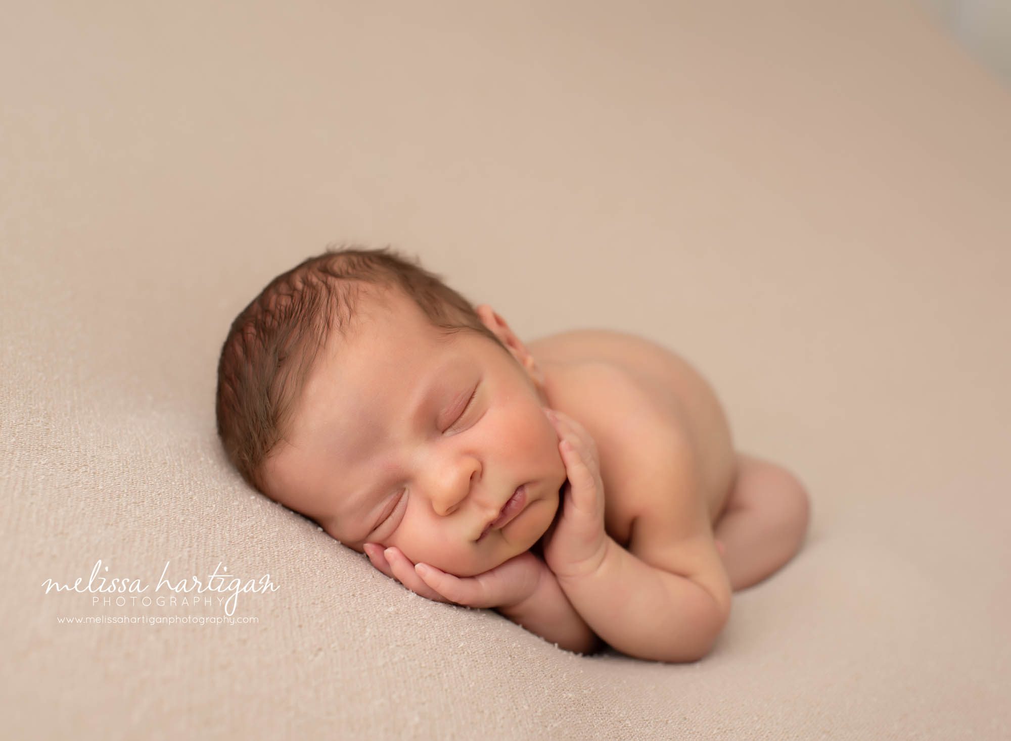 baby boy posed on side with hands under chin light tan colored backdrop posed newborn photography