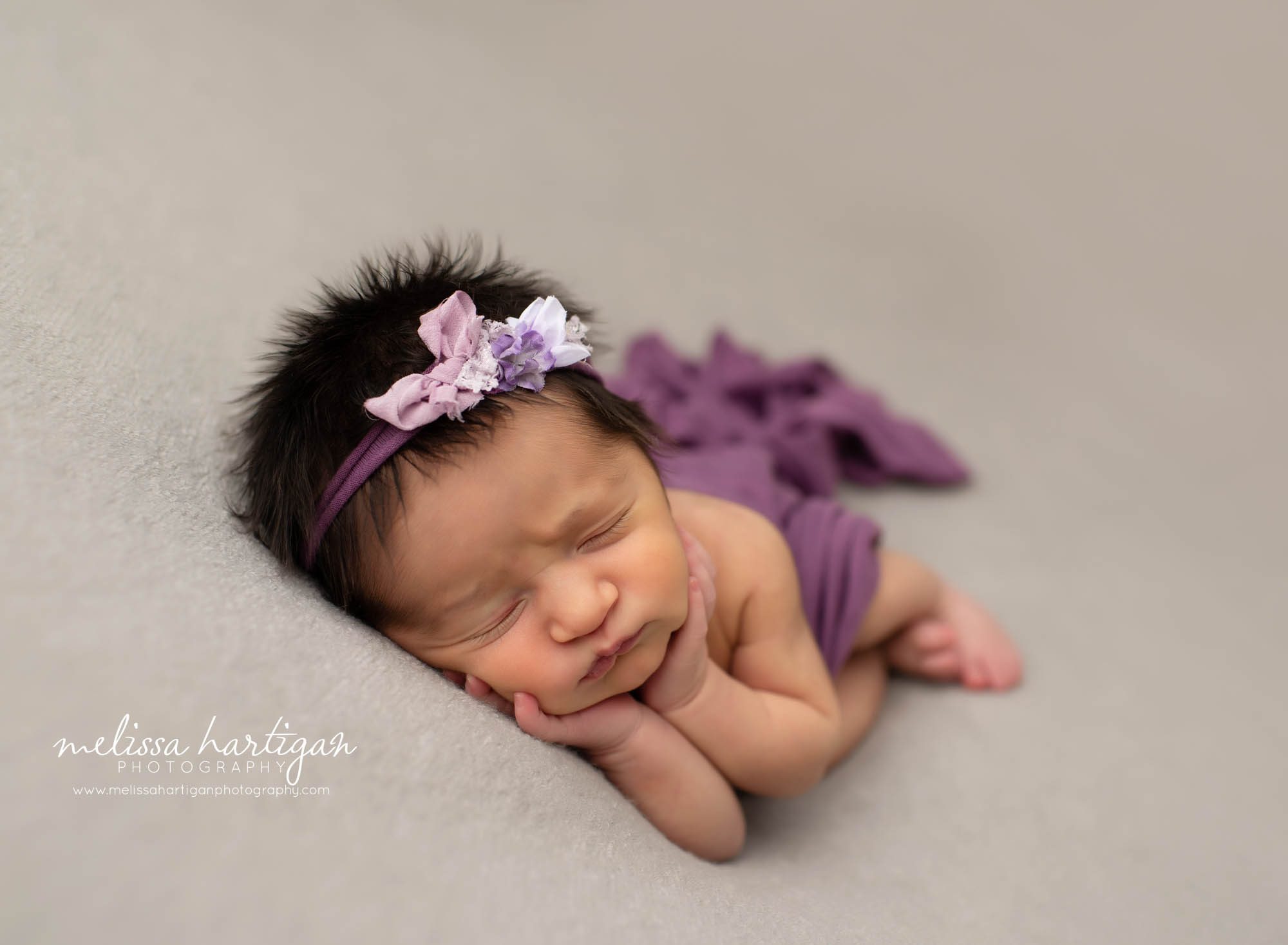 baby girl laying on side with hands under chin with purple wrap and purple headband