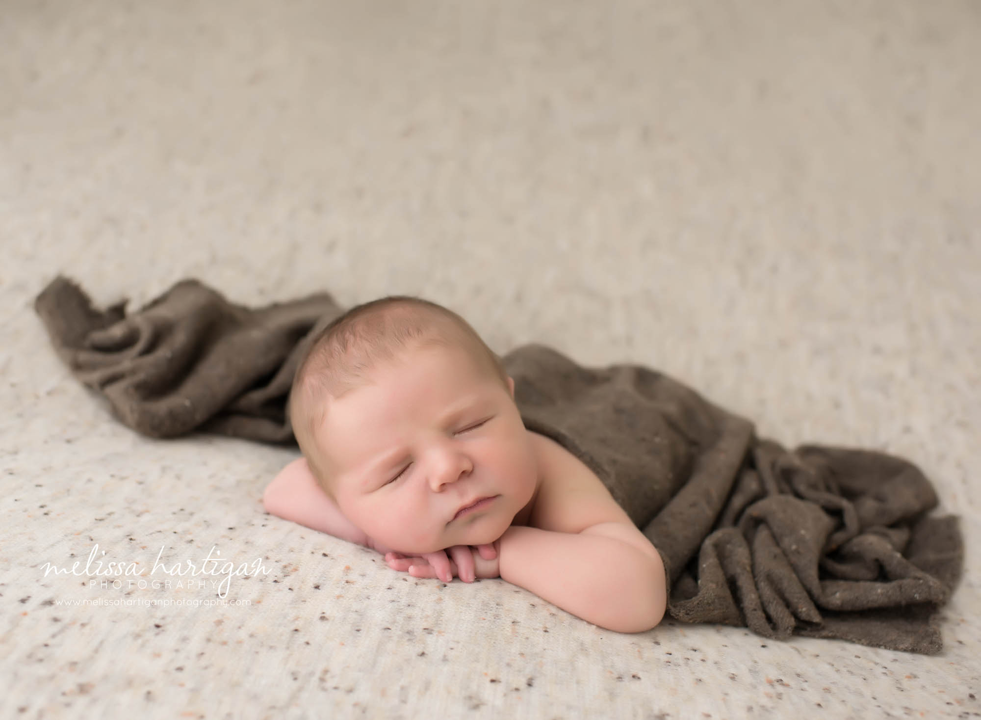 baby boy posed with chin resting on hands neutral colored backdrop