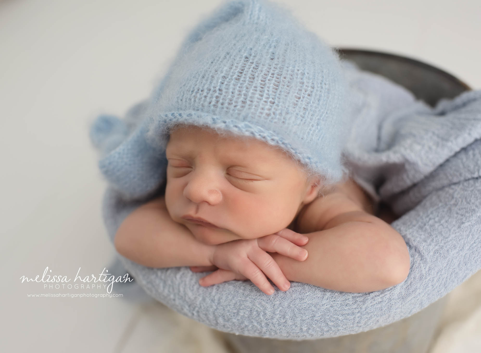 baby boy posed in bucket with light baby blue knitted sleepy cap
