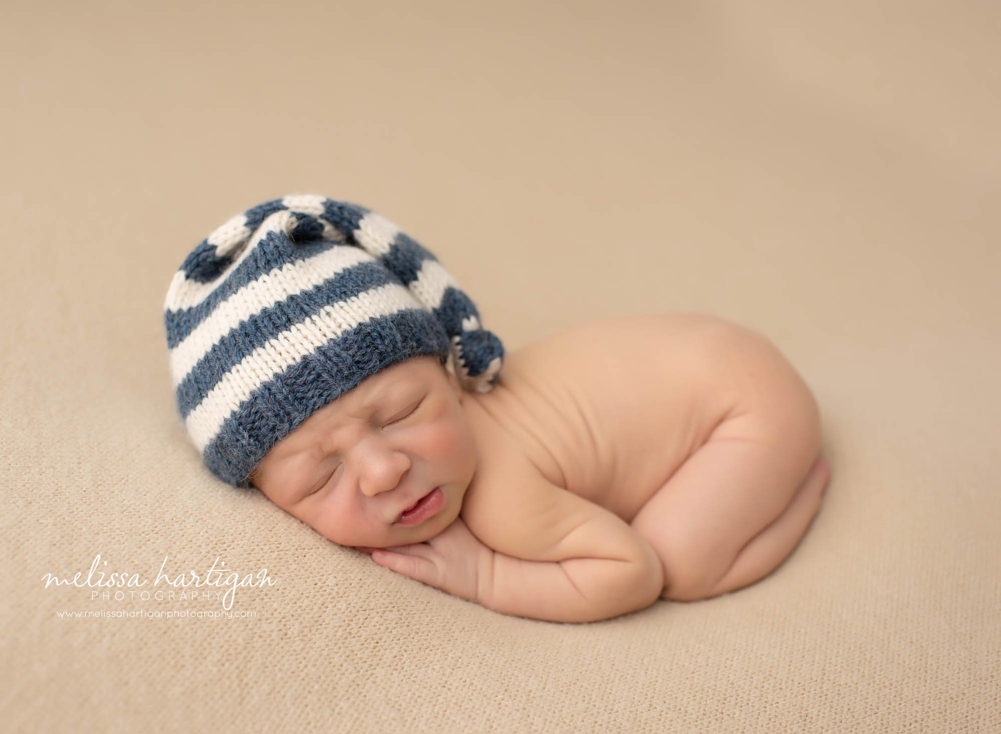 newborn on light colored backdrop with cream and blue striped knitted newborn hat