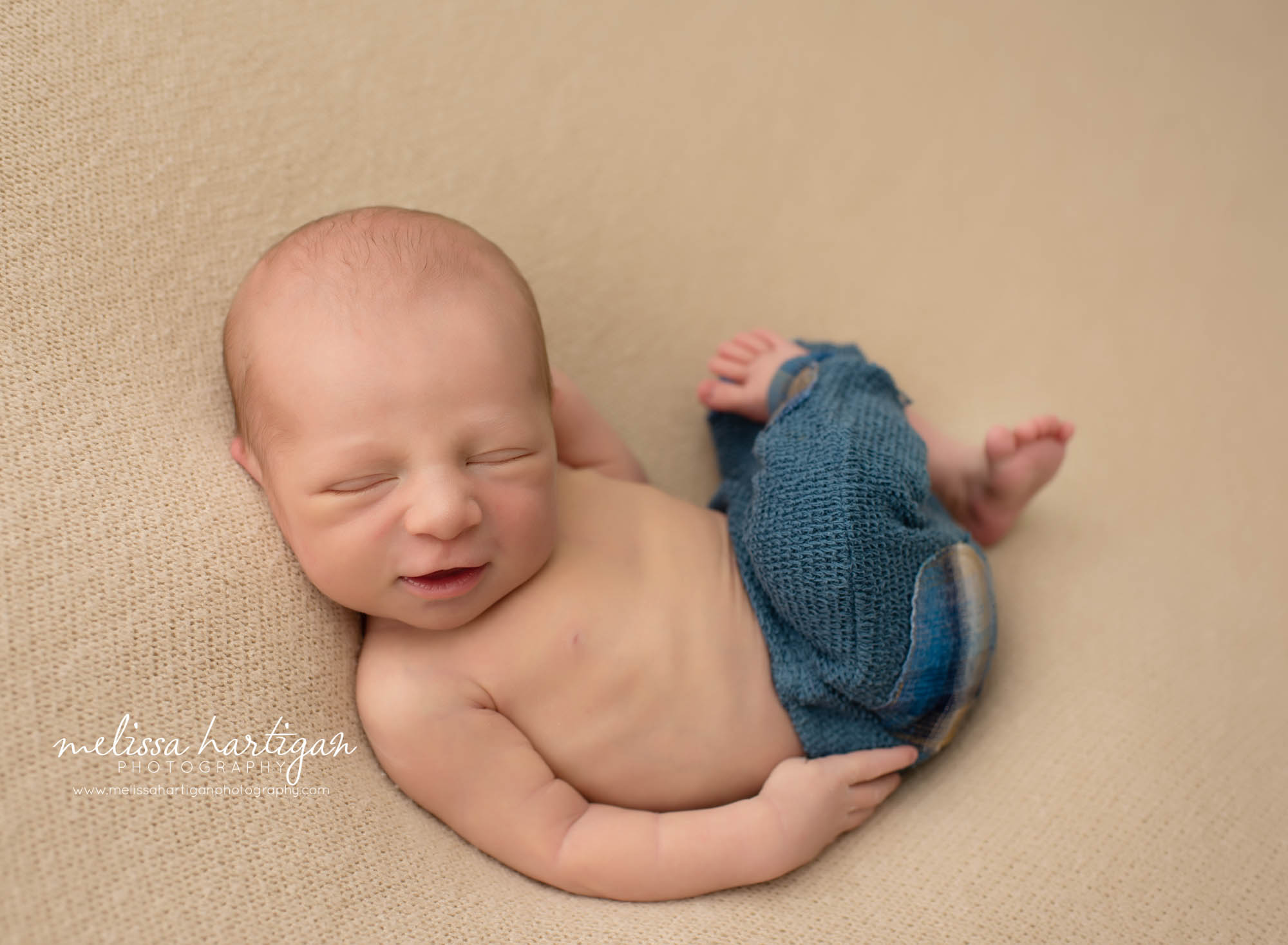 newborn wearing blue pants posed curled on backrop