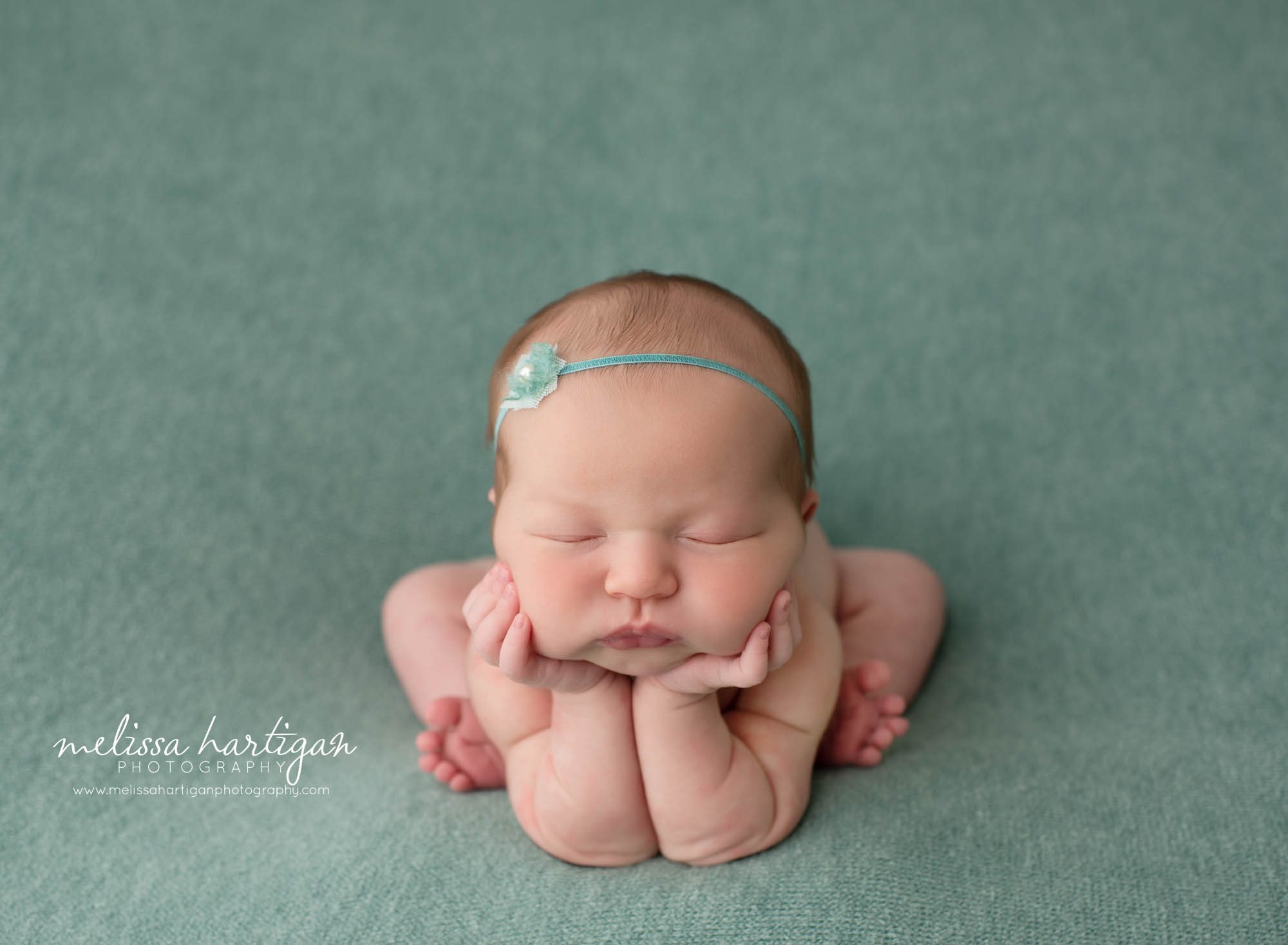 Baby girl in froggy pose on teal colored backdrop