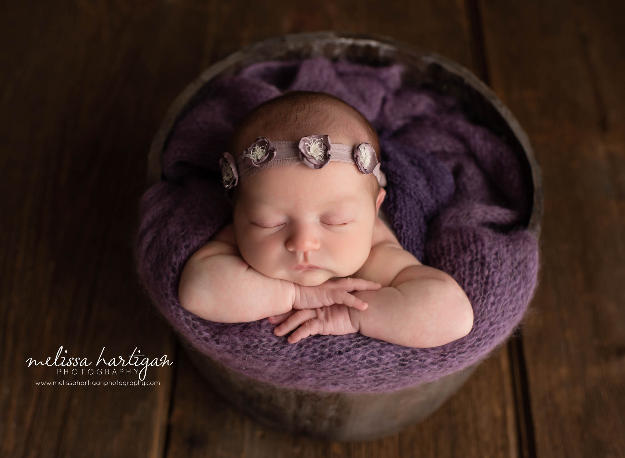 Baby girl posed in bucket woth purple wrap and purple flower headband